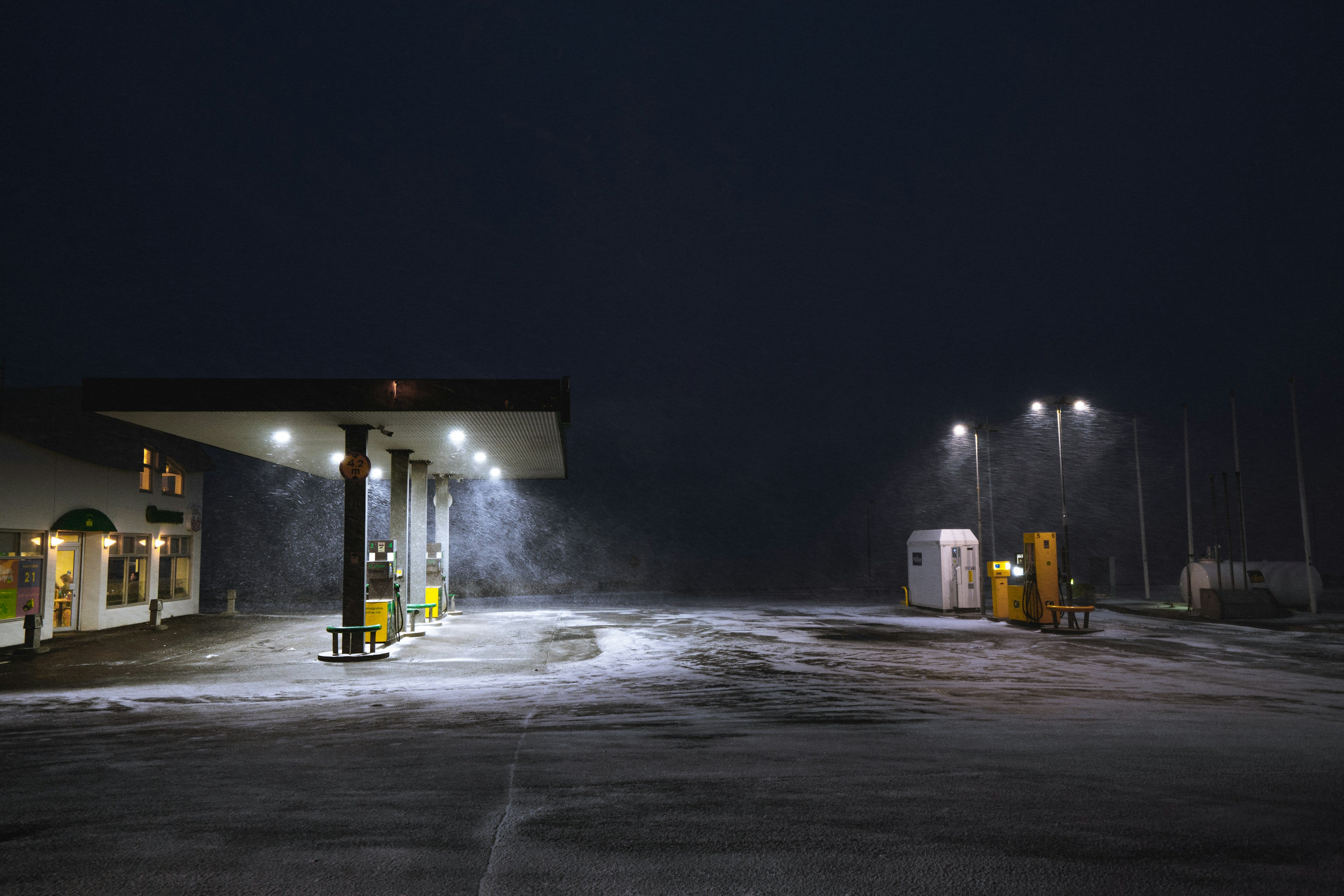 A lit petrol station forecourt at night with snow on the ground and nobody around