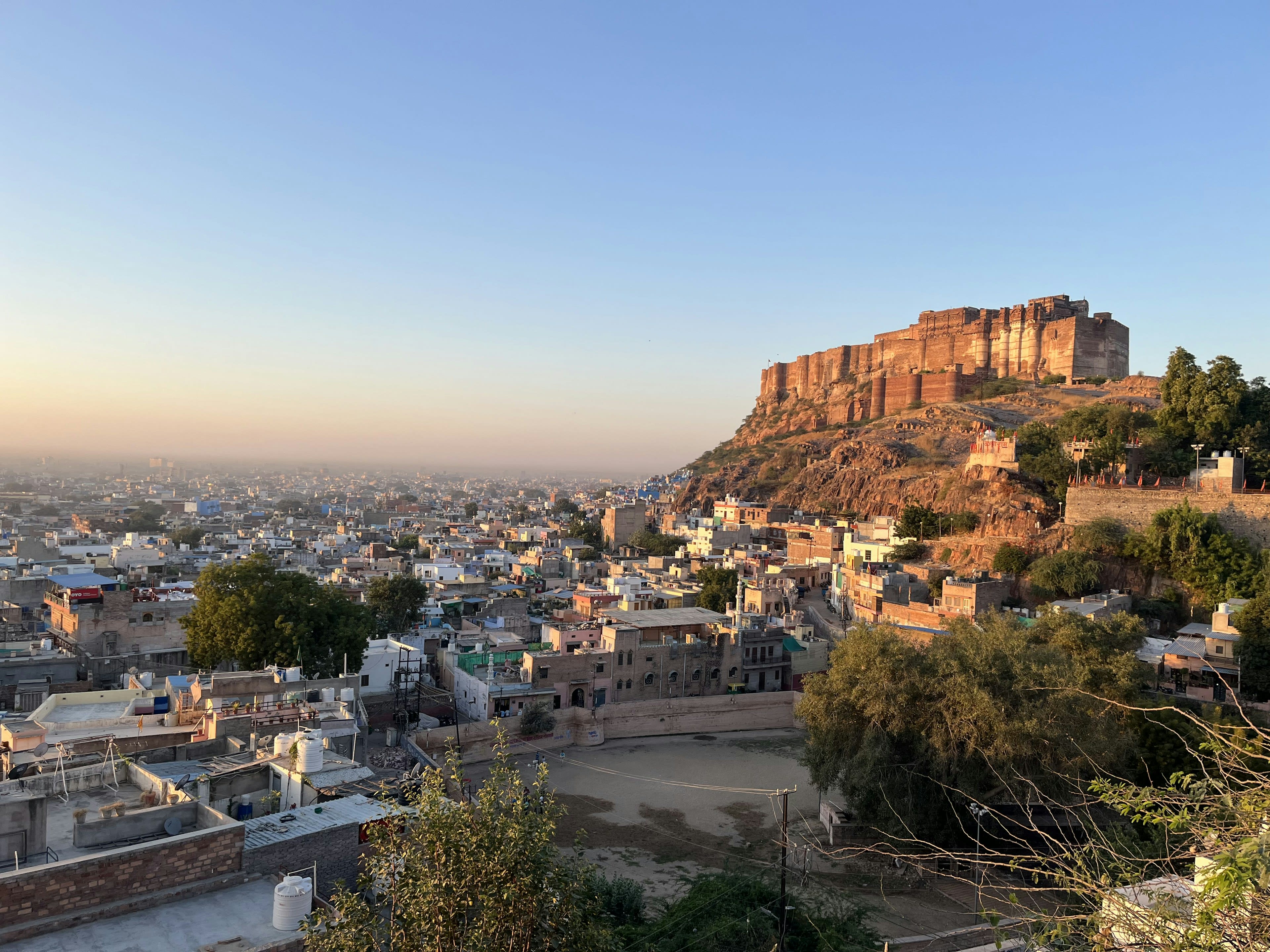 A massive hilltop fort glowing at dusk above a sprawling city