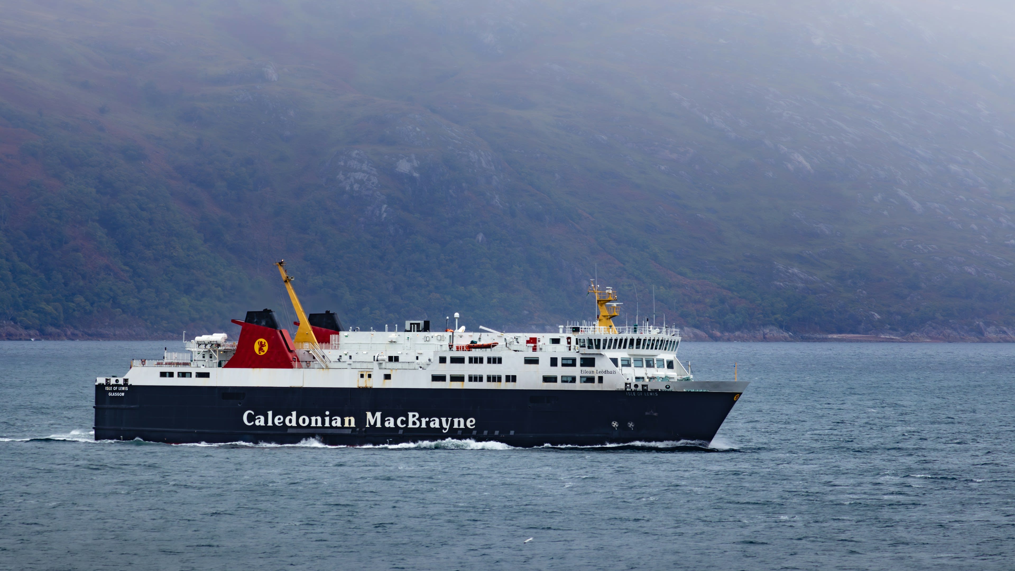 A Caledonian MacBrayne ferry crossing grey water with hills behind