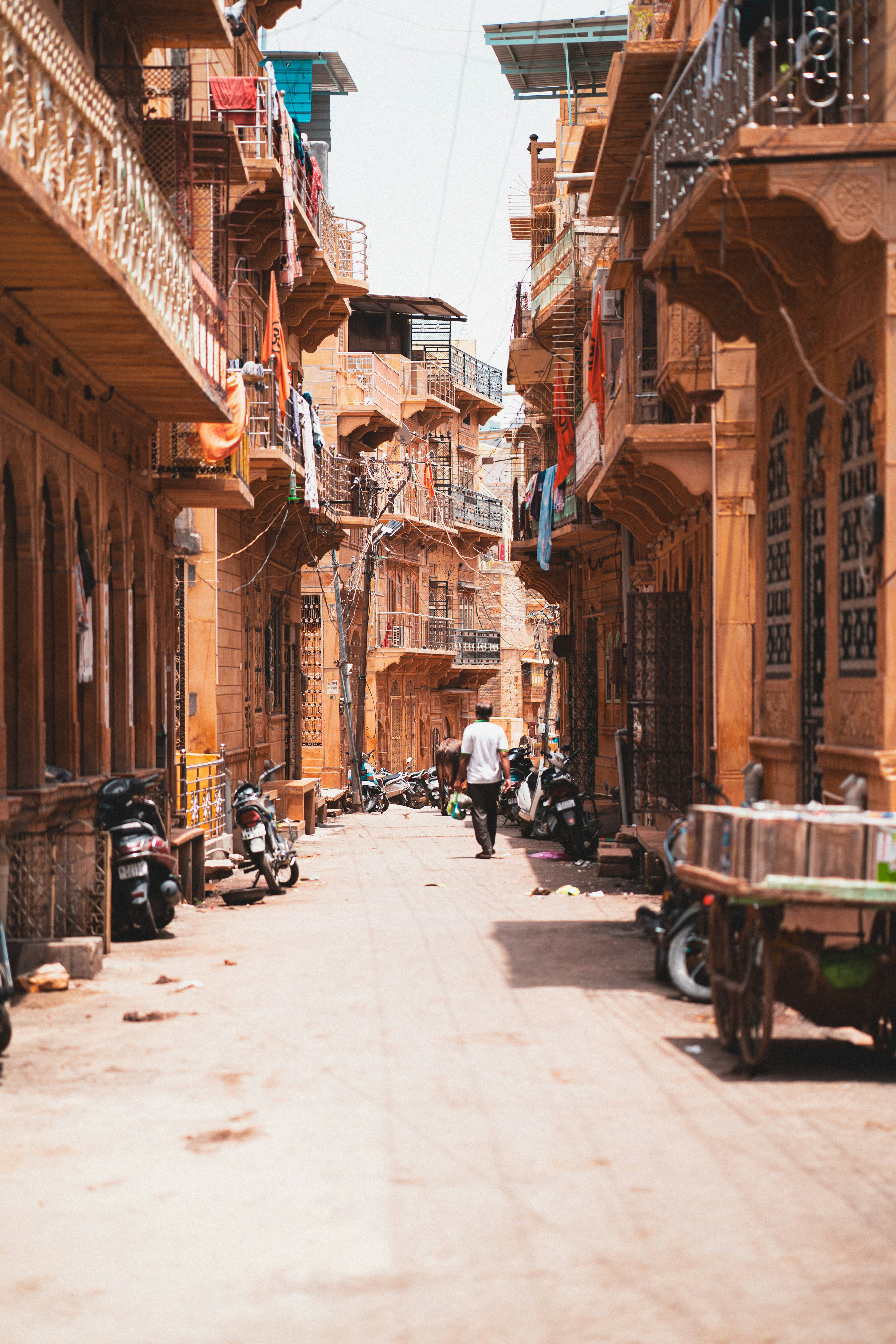 A narrow street between carved sandstone buildings lined with parked motorcycles