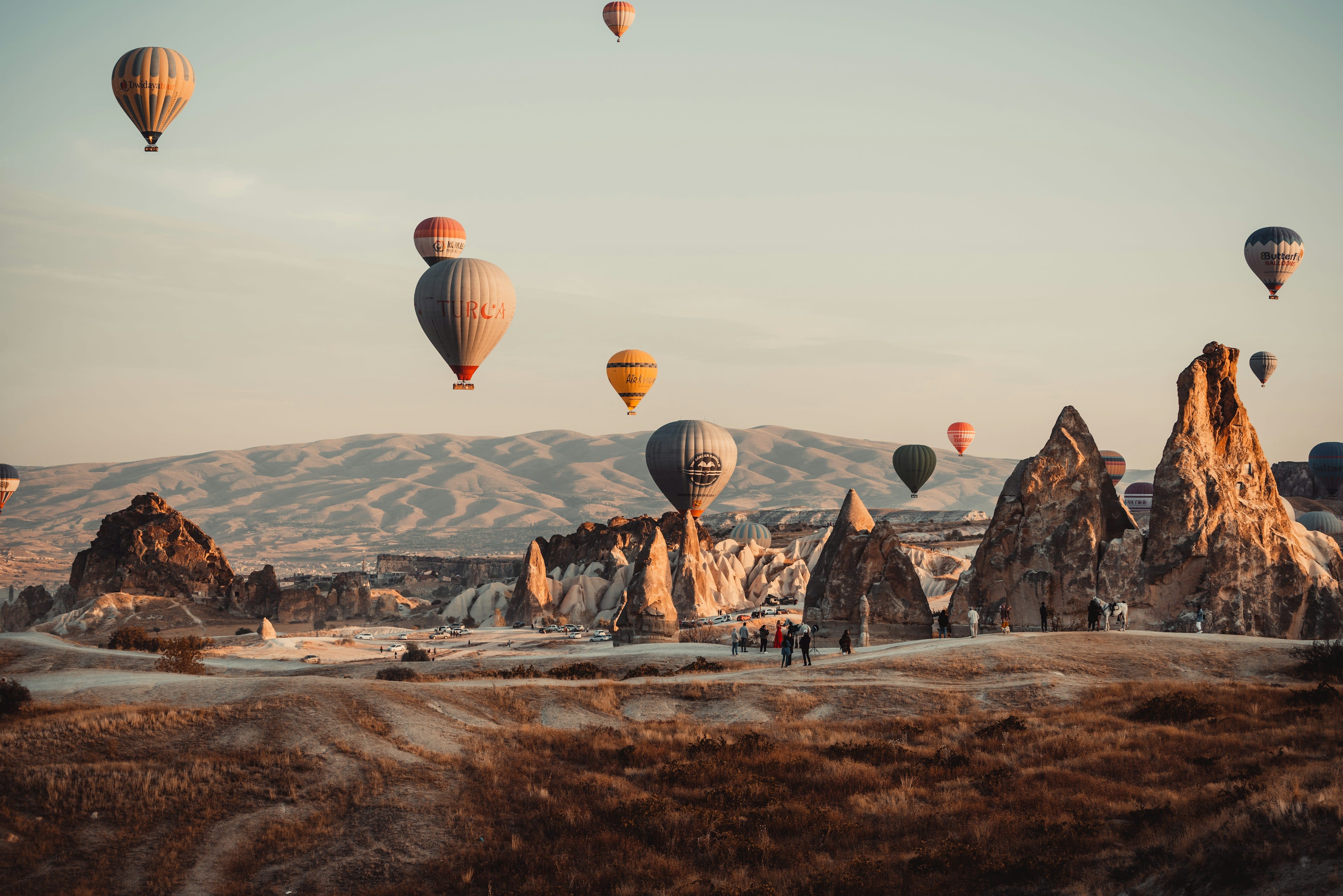 Dozens of hot air balloons rising over a rocky valley at dawn