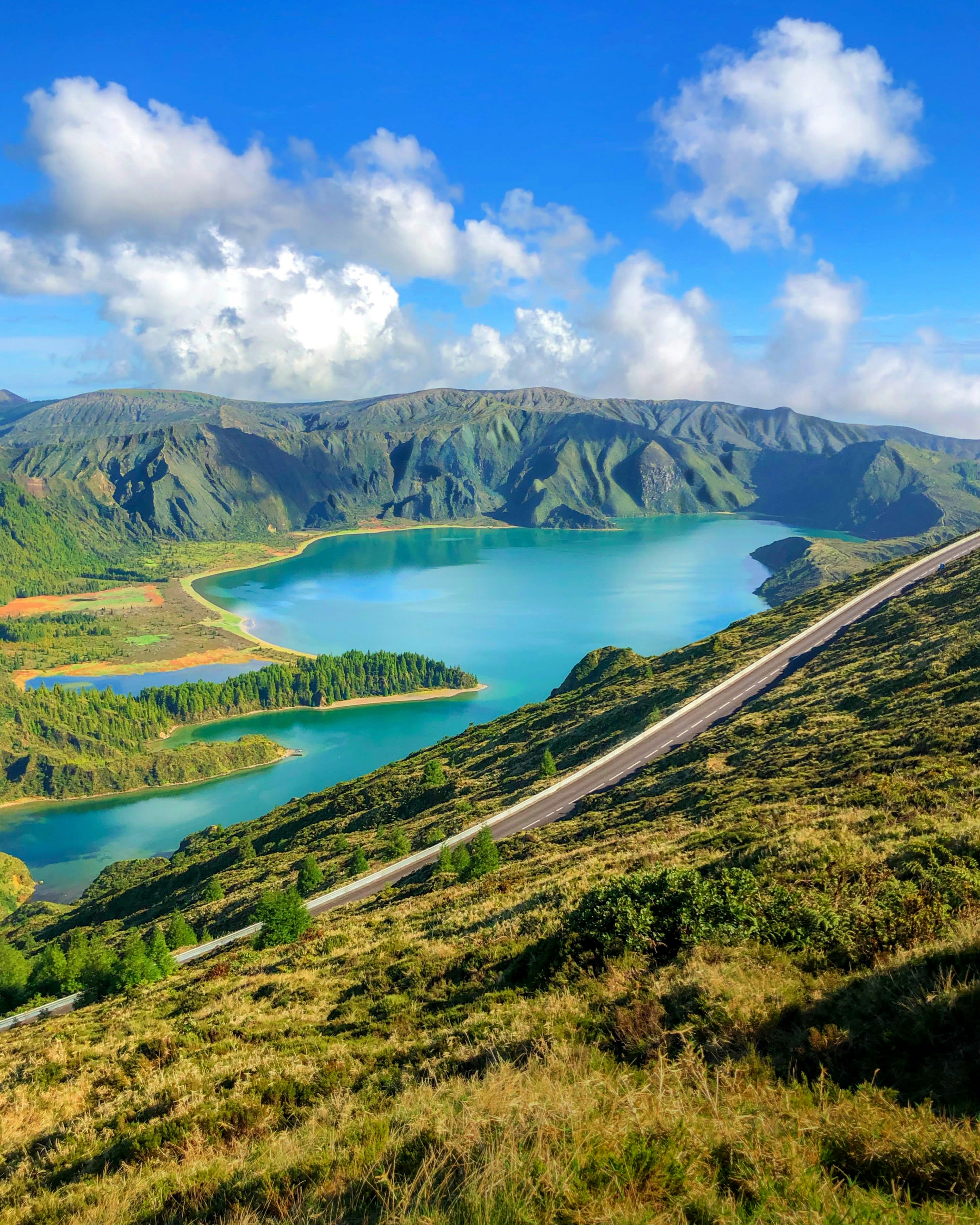 A turquoise crater lake seen from a steep green rim under blue sky