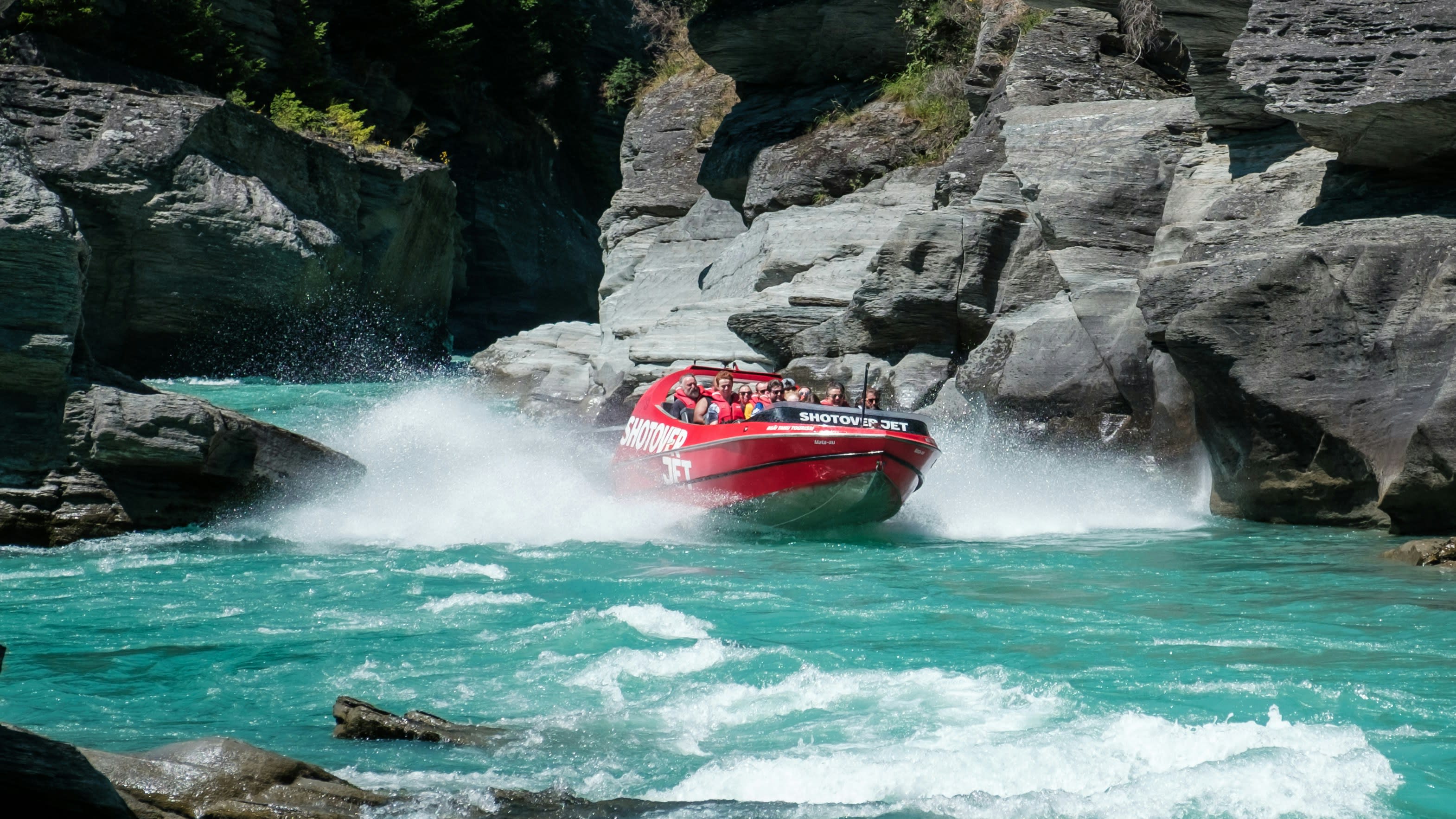A red jet boat throwing spray as it turns hard in a rocky river canyon