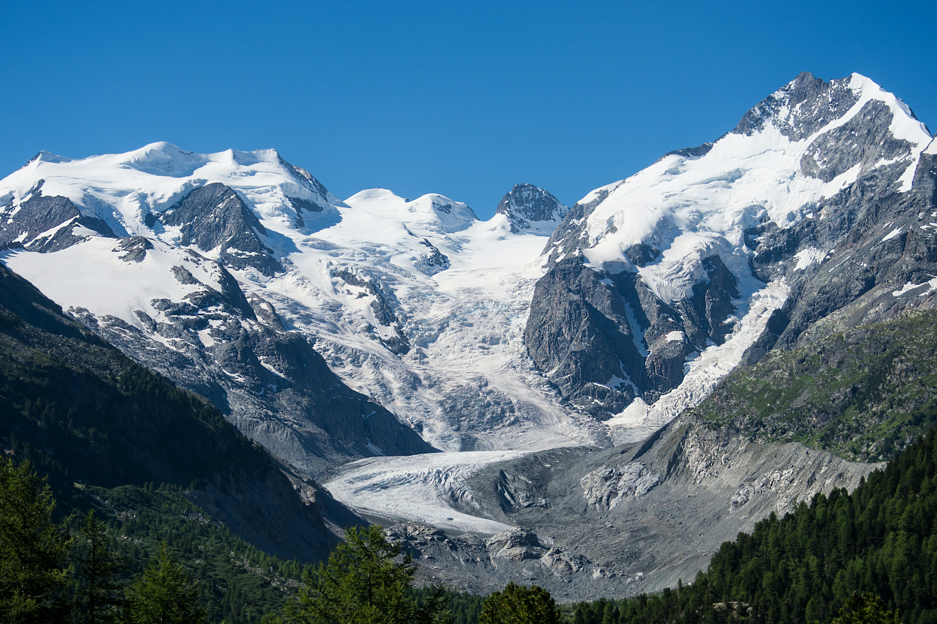A glacier descending between snow-covered peaks under blue sky