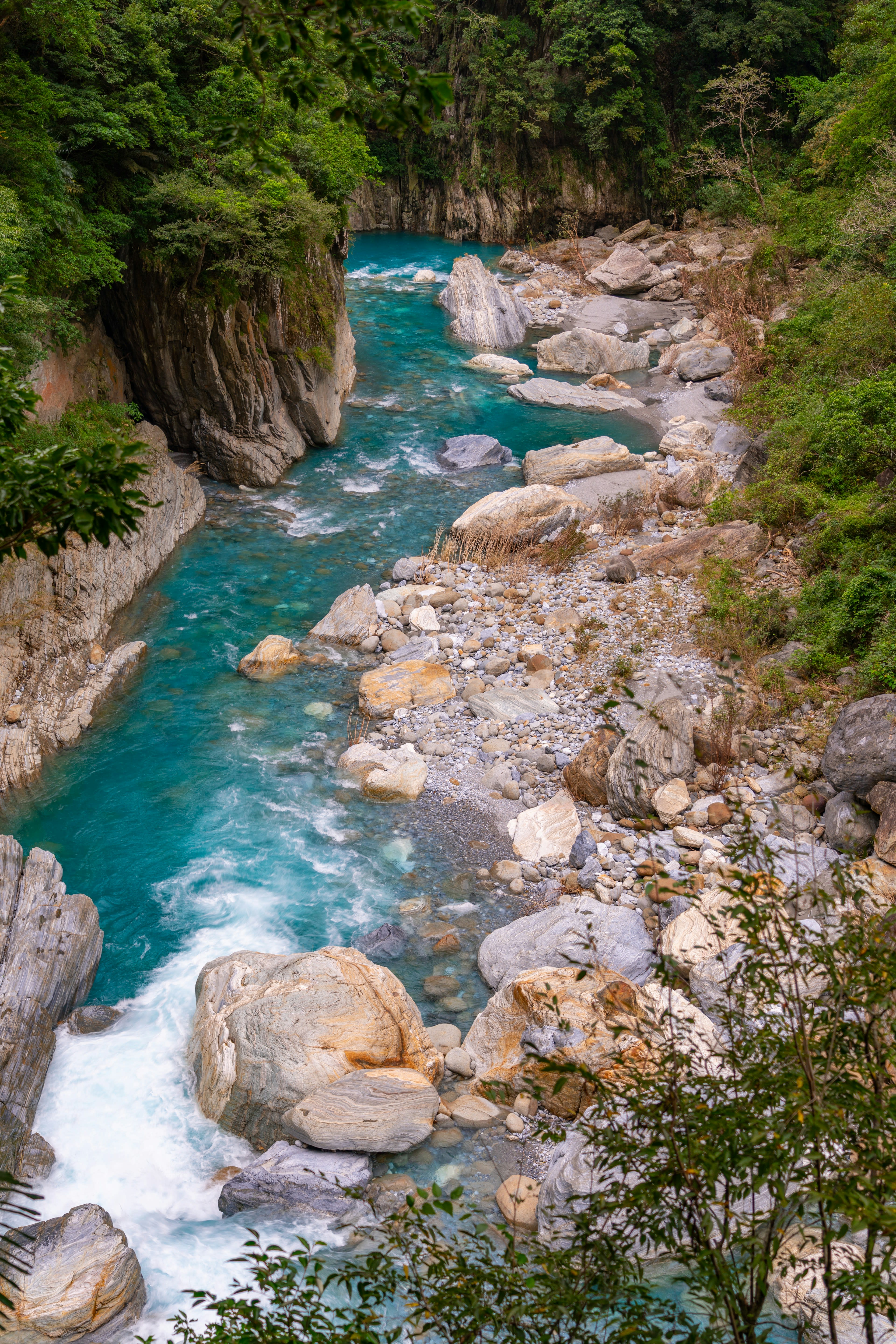 A turquoise river running between pale boulders below green cliffs