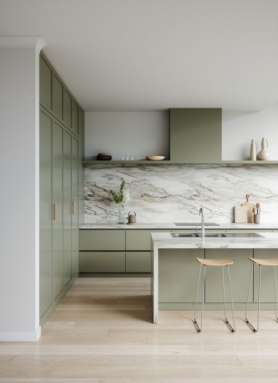 Sage green kitchen with full-height cupboards, a marble splashback and oak stools