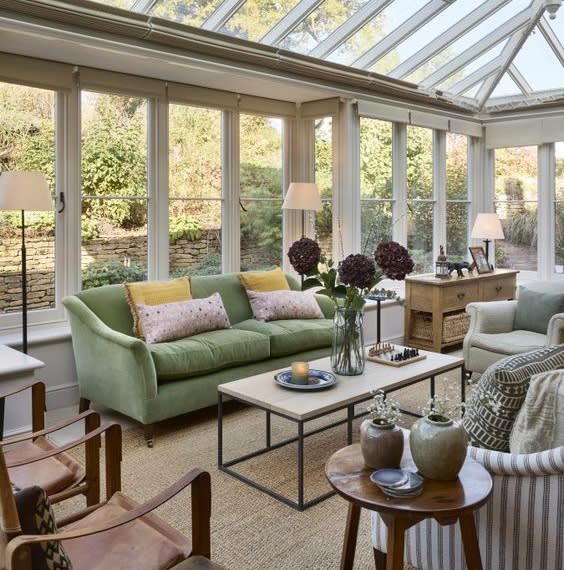 Conservatory with a green sofa, glass roof and a coffee table set for tea