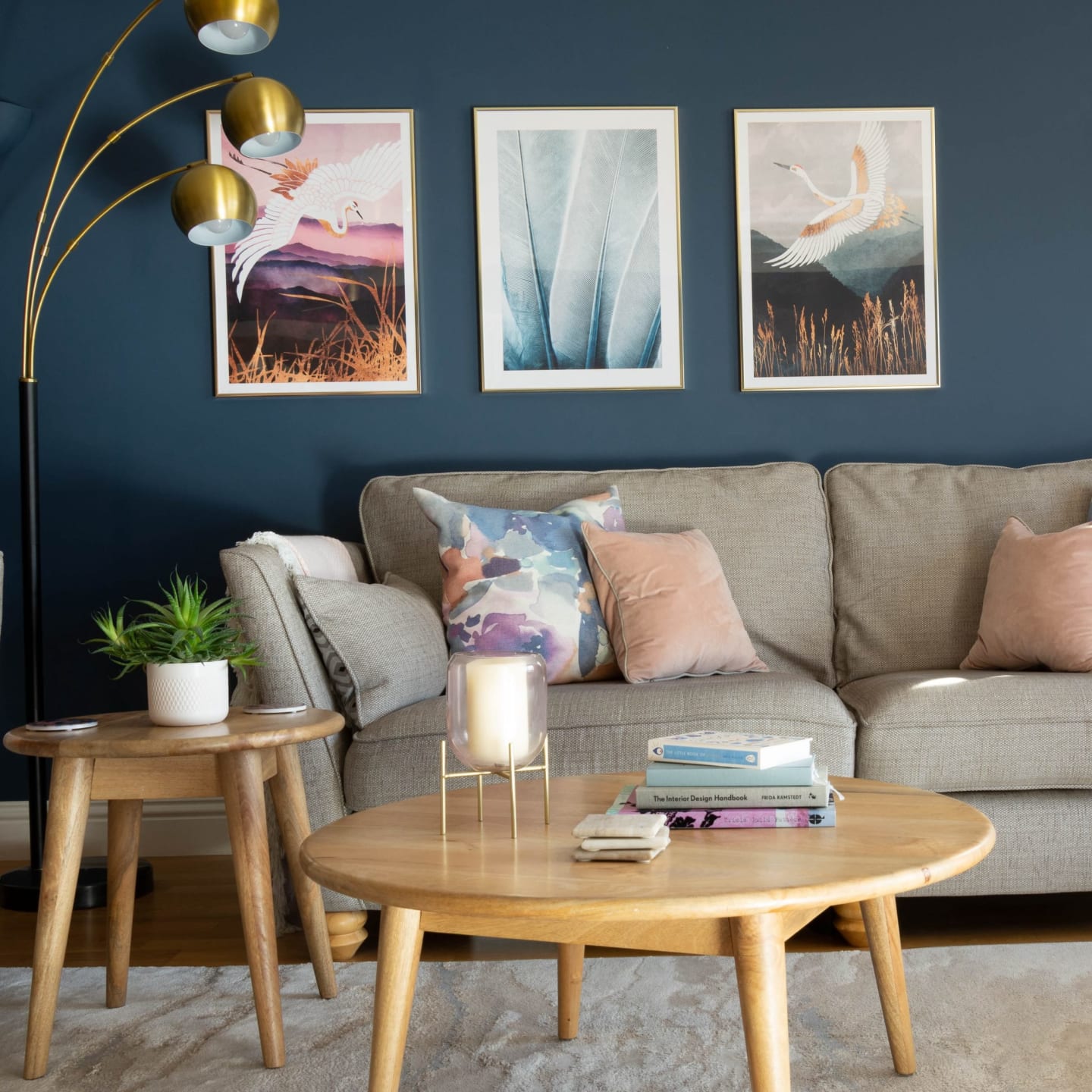 Grey sofa against a navy wall with three framed prints and a brass arc floor lamp