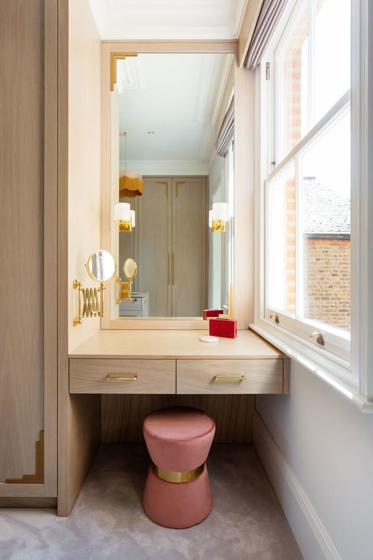 Dressing table in a window alcove with a pink stool and a wall light