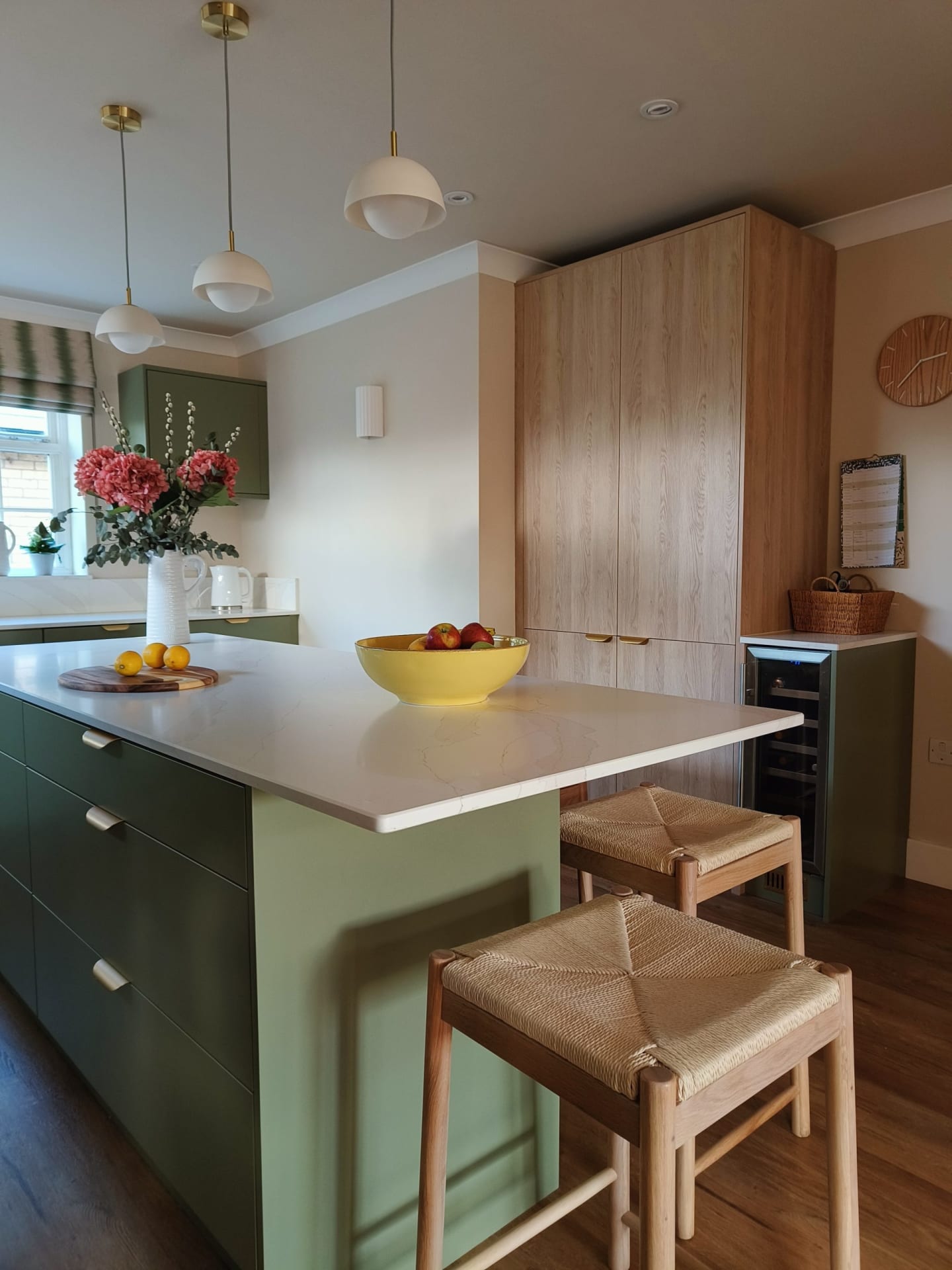 Green kitchen island with oak larder cupboards and brass pendant lights