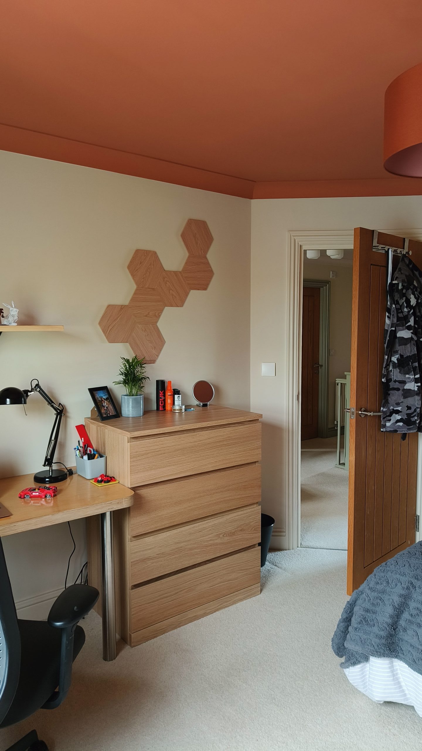 Oak chest of drawers and desk below hexagonal wall panels with a terracotta ceiling