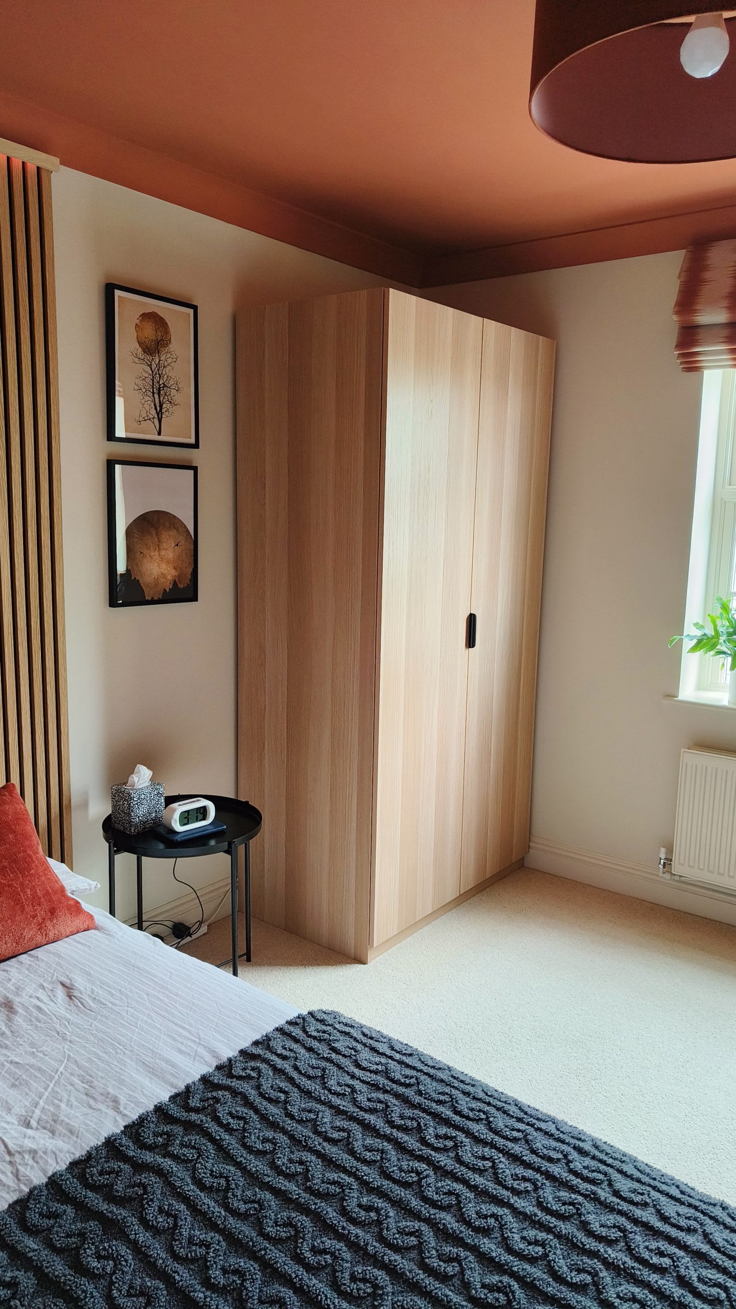 Oak corner wardrobe beside framed botanical prints and slatted wood panelling