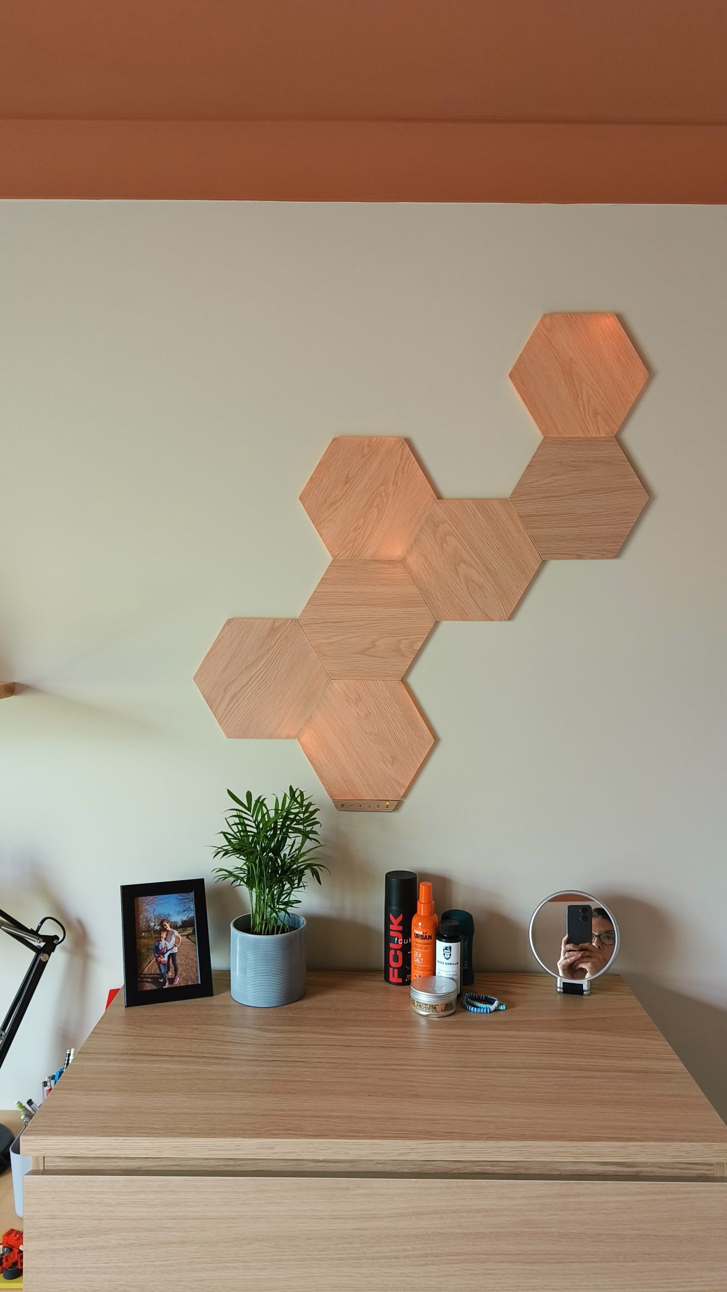 Hexagonal oak wall tiles above a desk with a potted plant and framed photograph