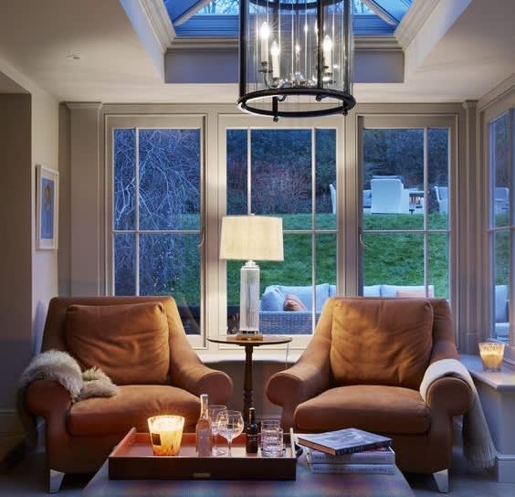 Two tan leather armchairs beside garden windows under a lantern pendant light