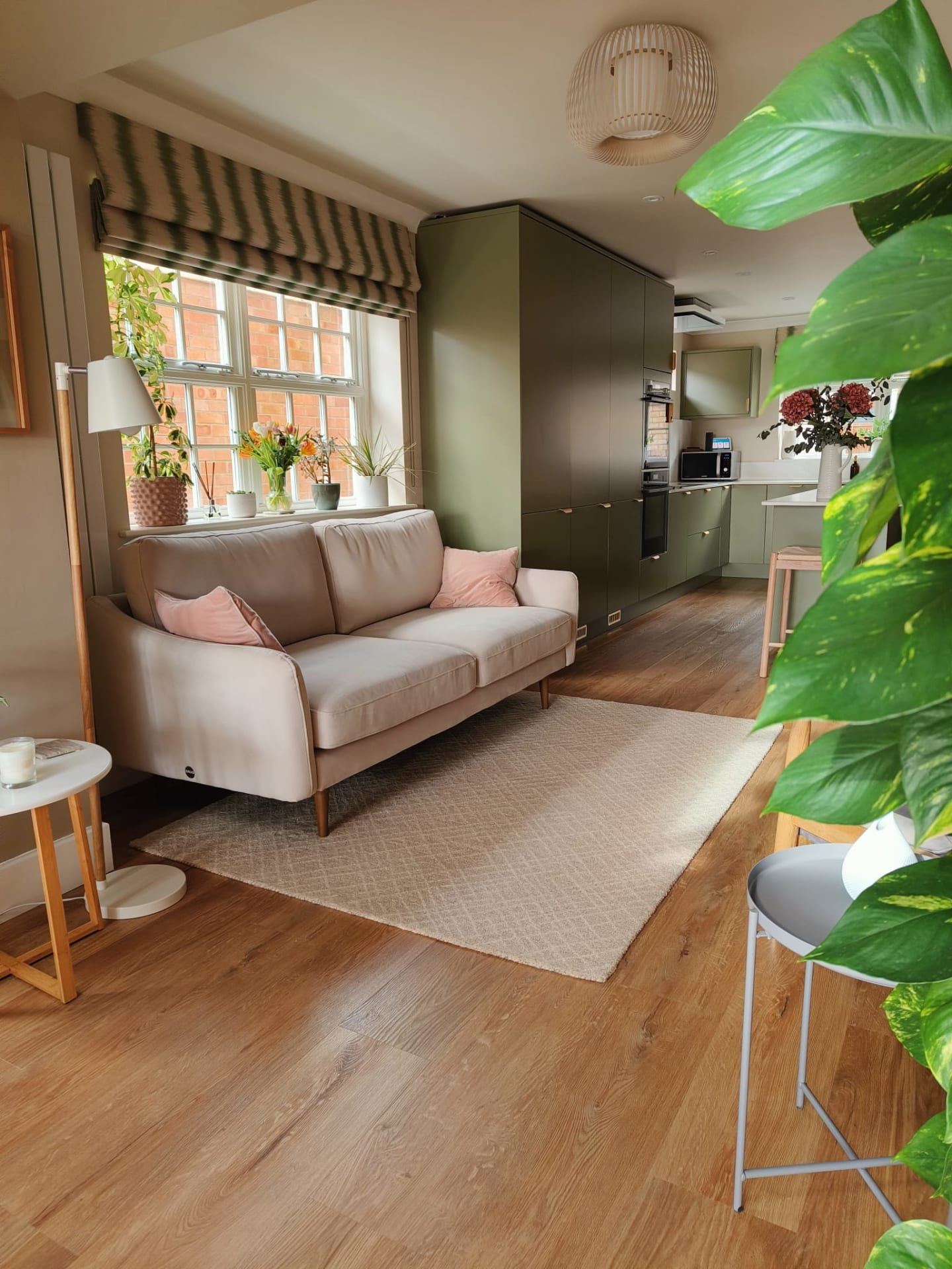 Pale pink sofa in the snug looking through to green kitchen cabinetry