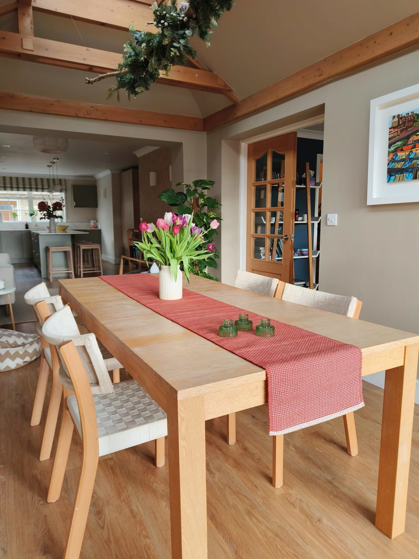 Oak dining table with a red runner and tulips beneath vaulted oak beams