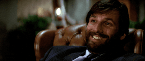 Ellis from Die Hard laughing in a chair