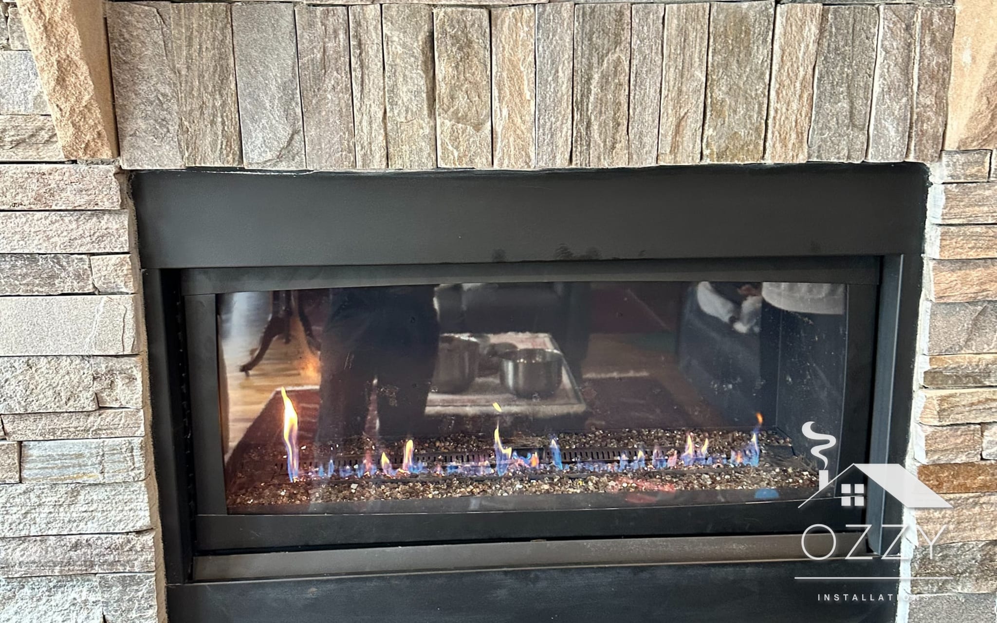 Linear gas fireplace with a flame running, set in a stacked stone wall