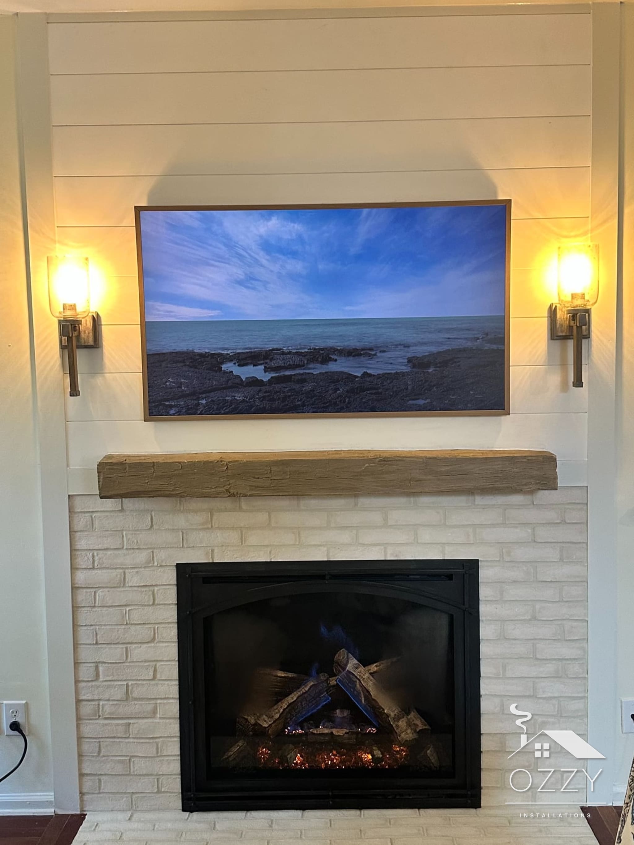 Finished gas fireplace in whitewashed brick under a beam mantel and shiplap wall