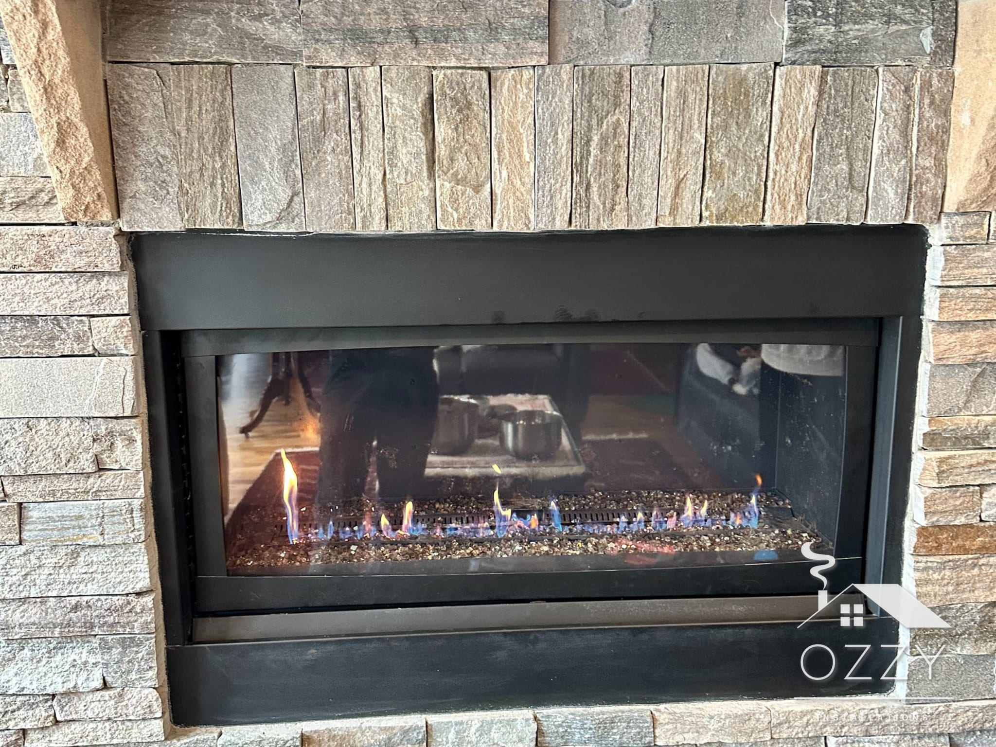 Linear gas fireplace with a flame running, set in a stacked stone wall