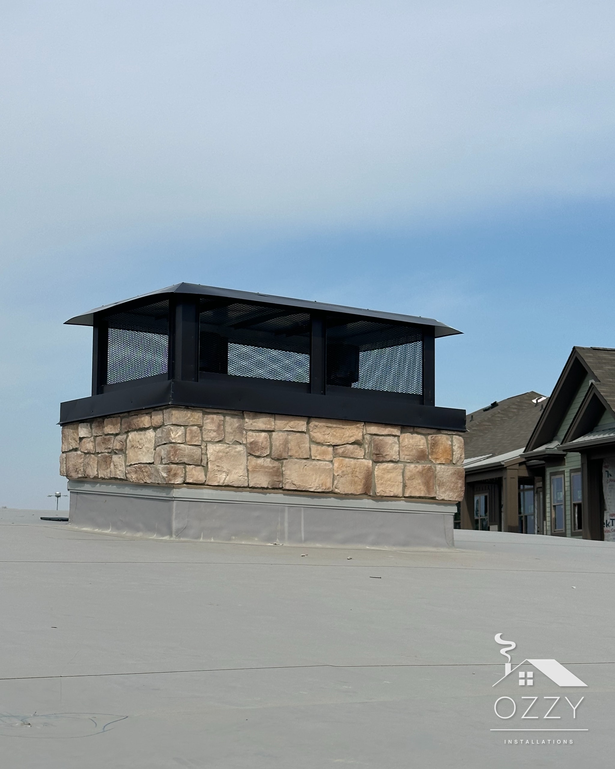 Stone chimney with a black decorative shroud on a commercial rooftop