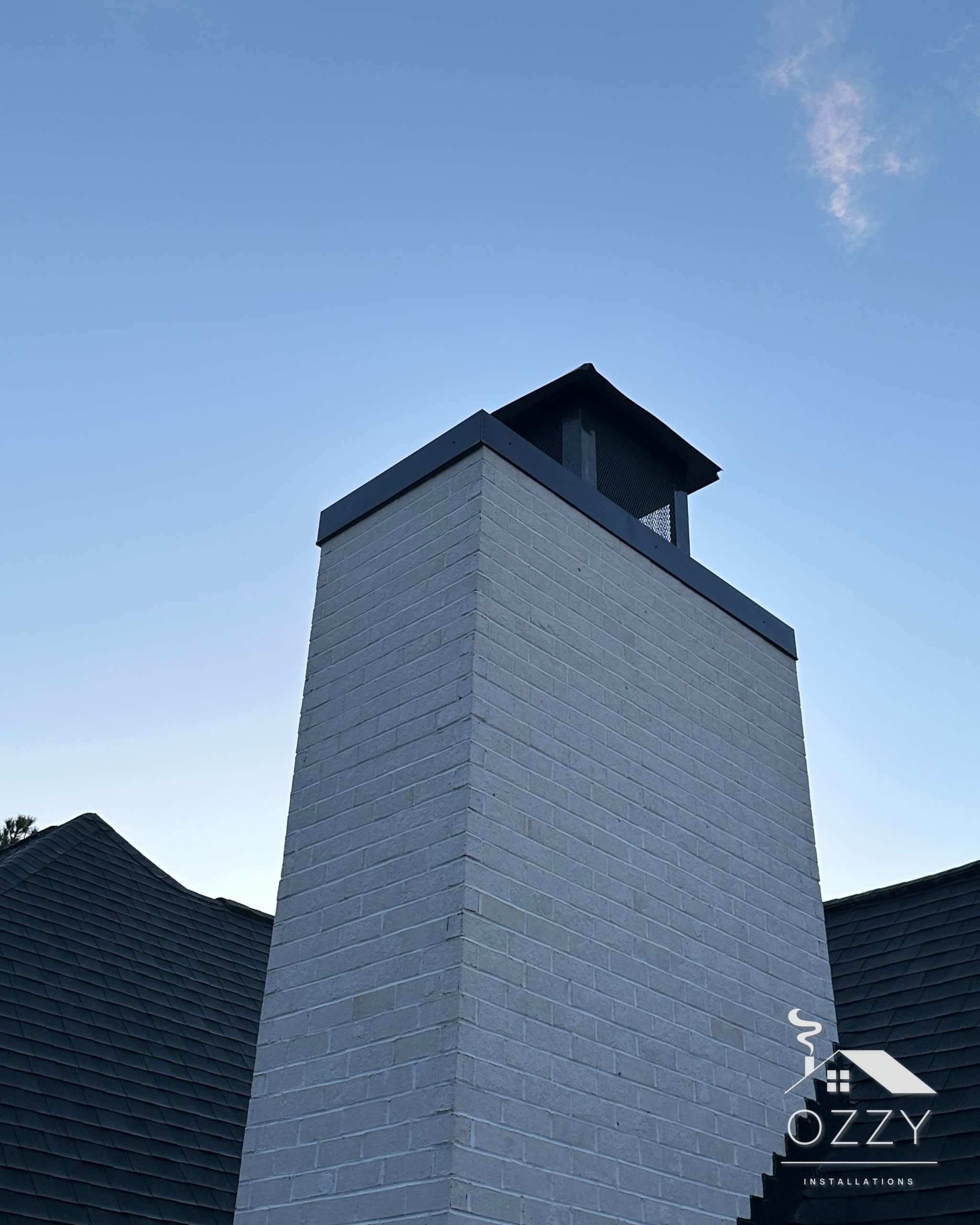 Painted white brick chimney with a black metal shroud at dusk
