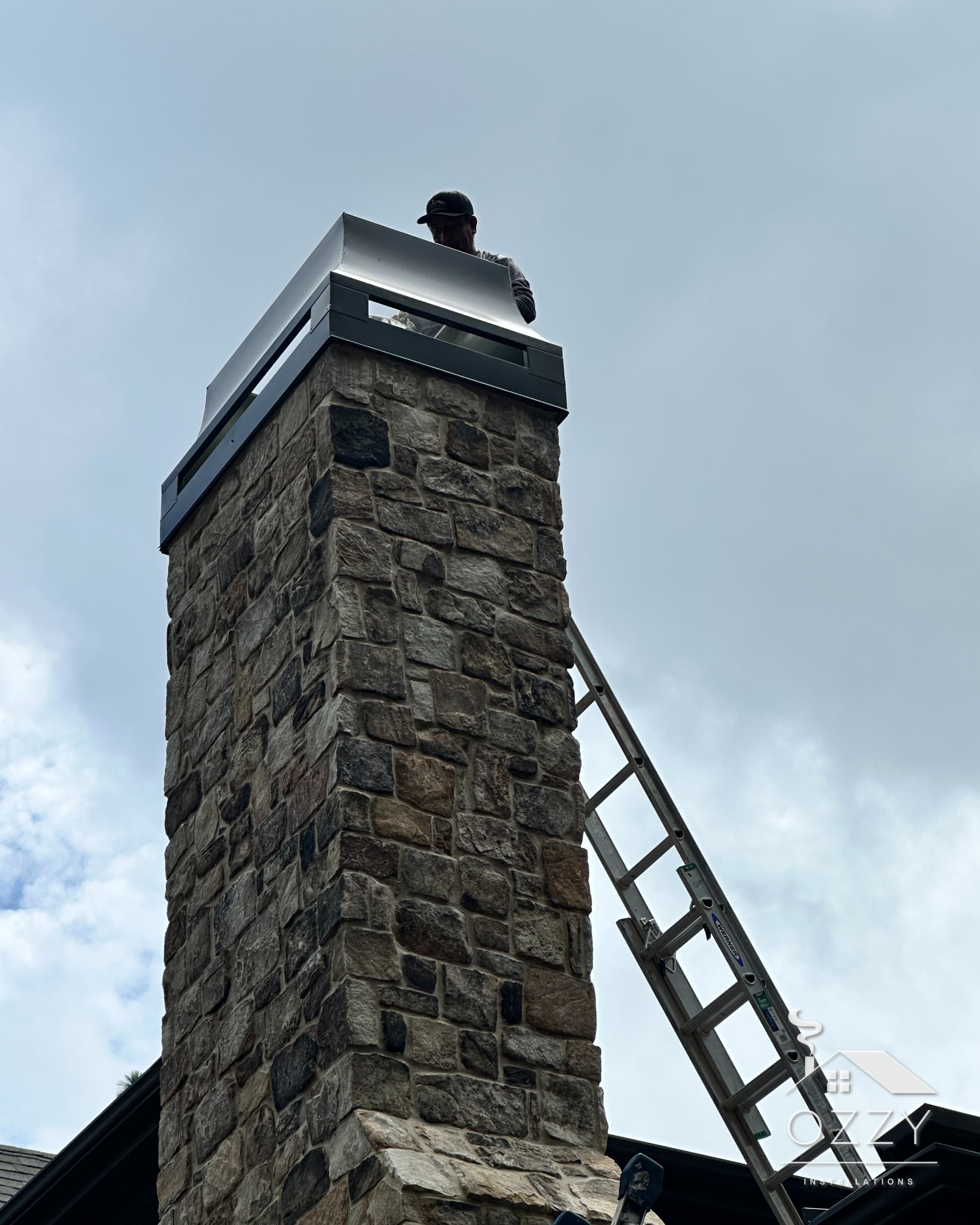 Tall stone chimney topped with a stainless steel chase cover and cap