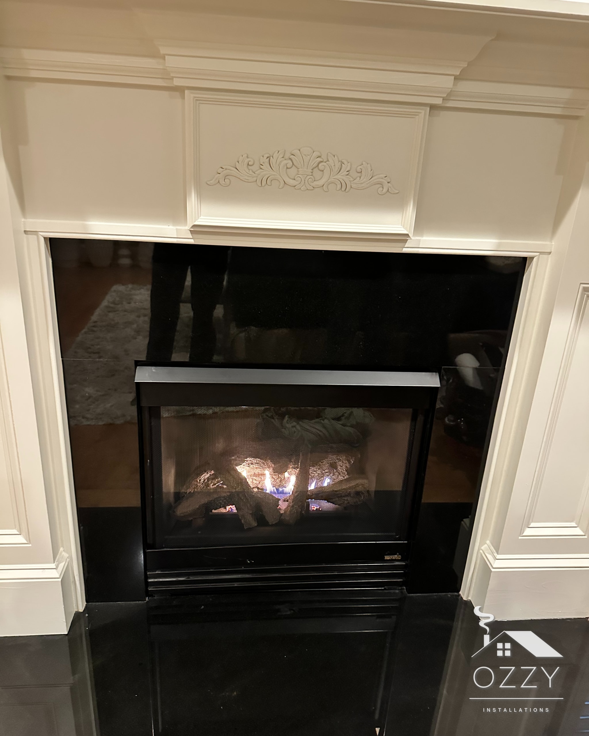 Lit gas insert set in a carved white mantel with black stone surround