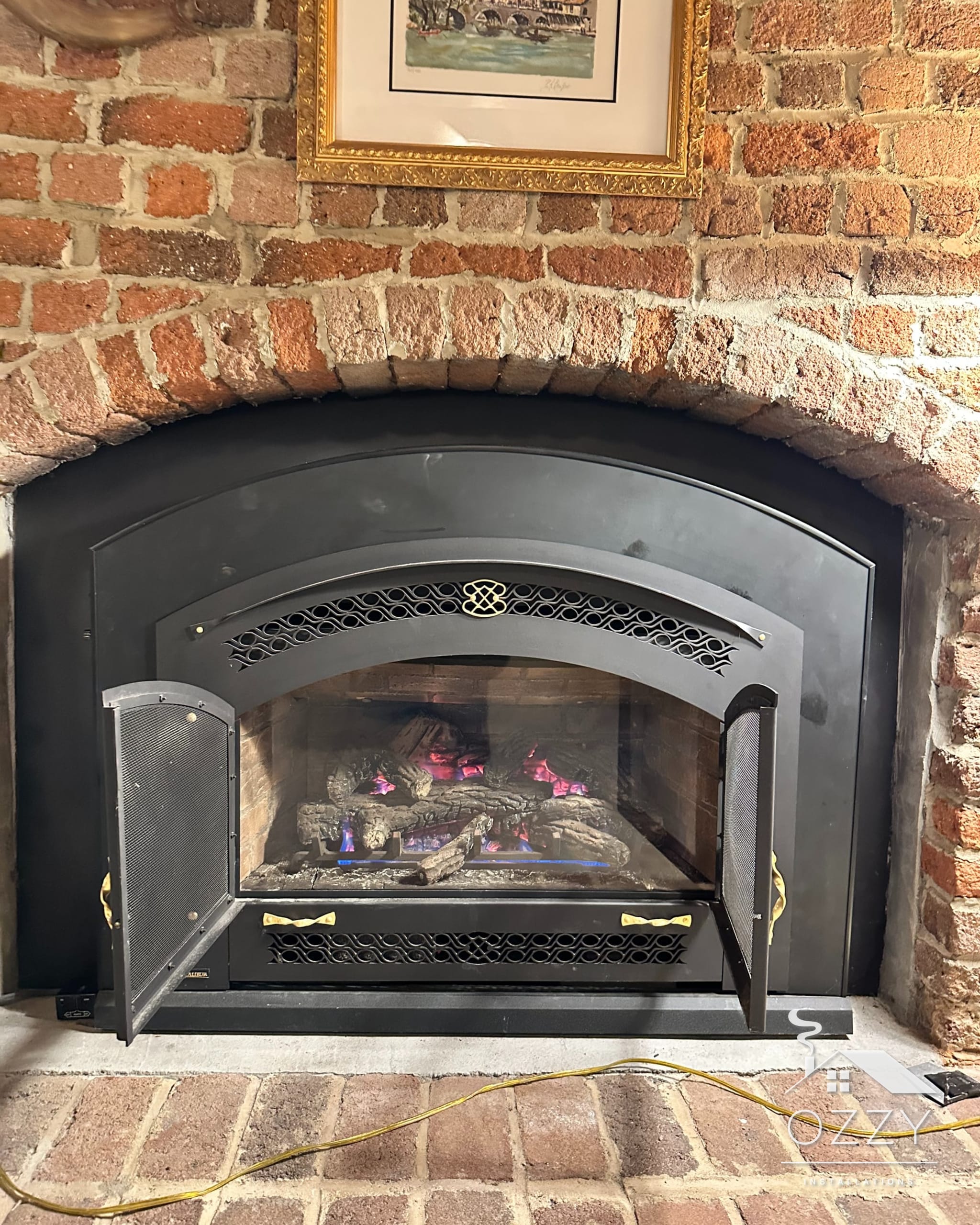 Arched black gas insert with the fire lit, set into a red brick fireplace