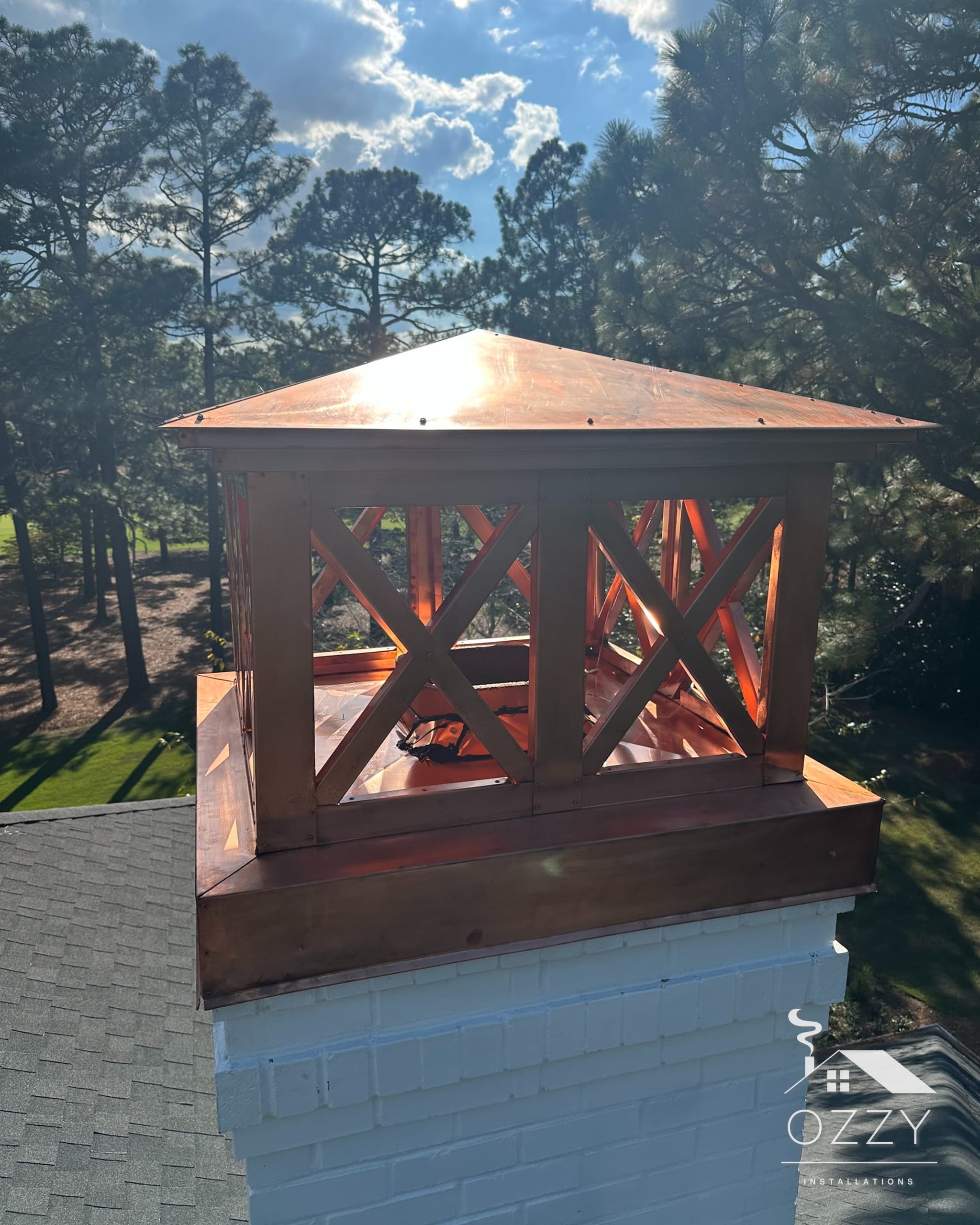 Copper chimney cap with cross-braced sides on a white chimney