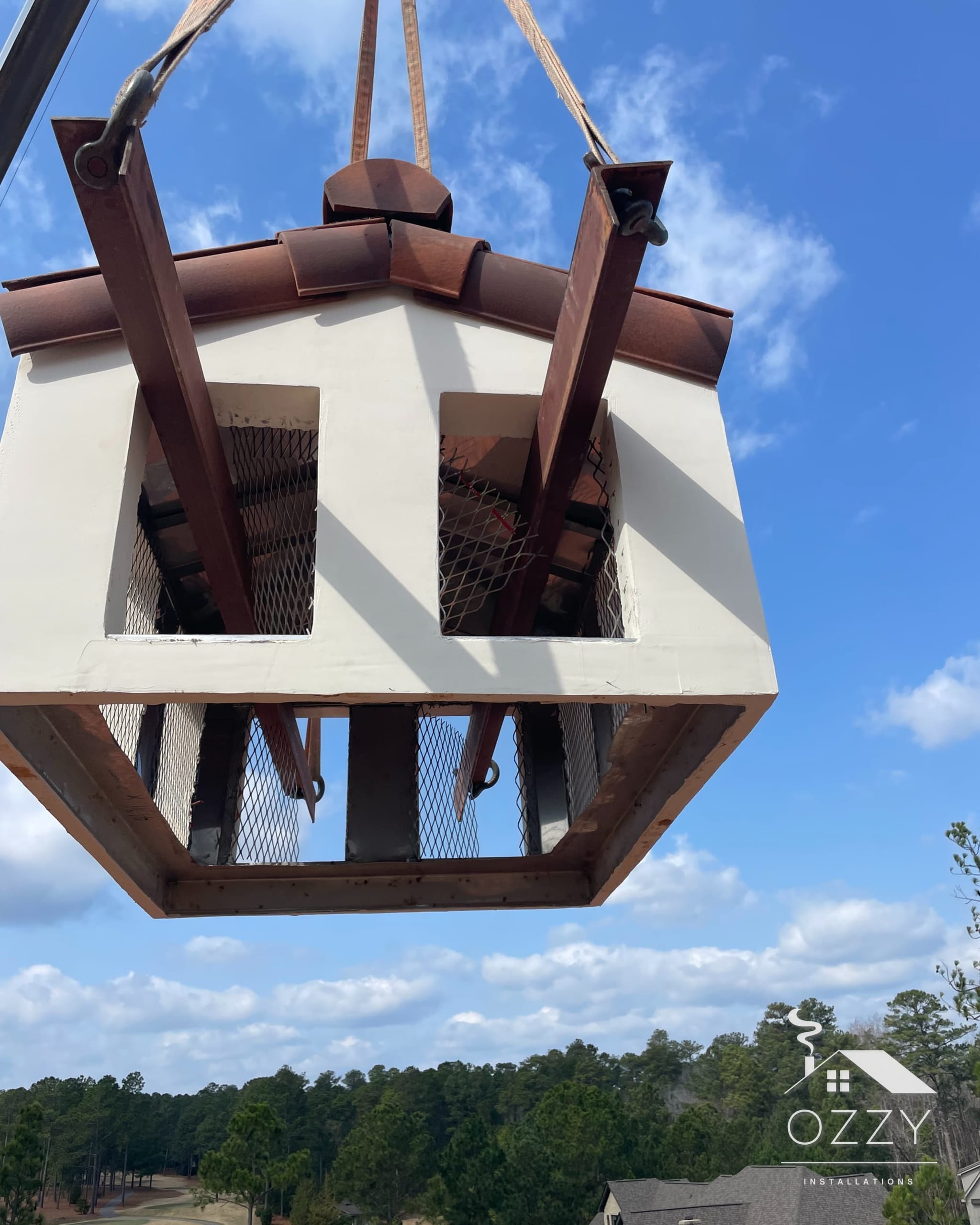 Custom chimney shroud hanging from crane straps against a blue sky