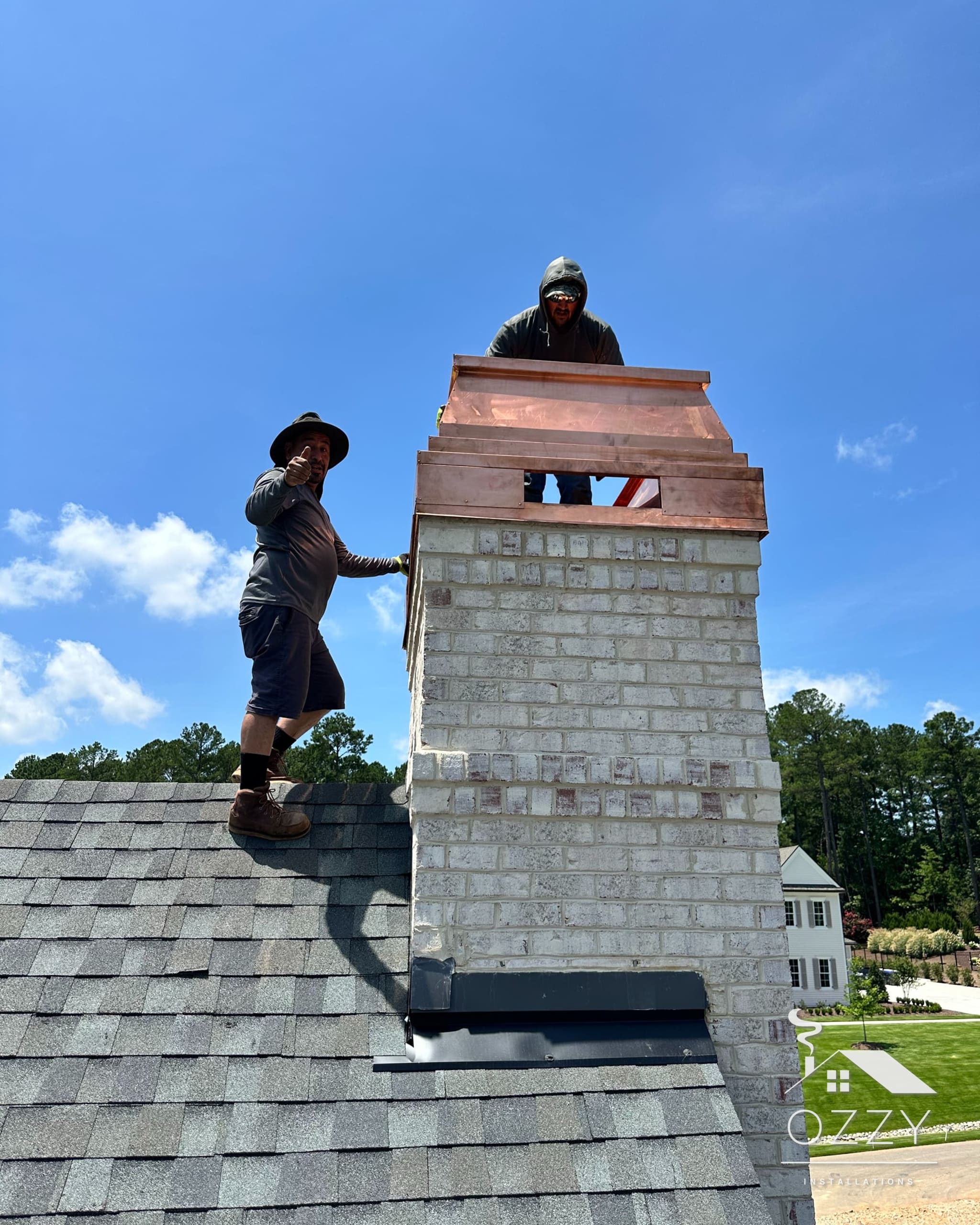 Two crew members setting a copper chimney cap on a roof