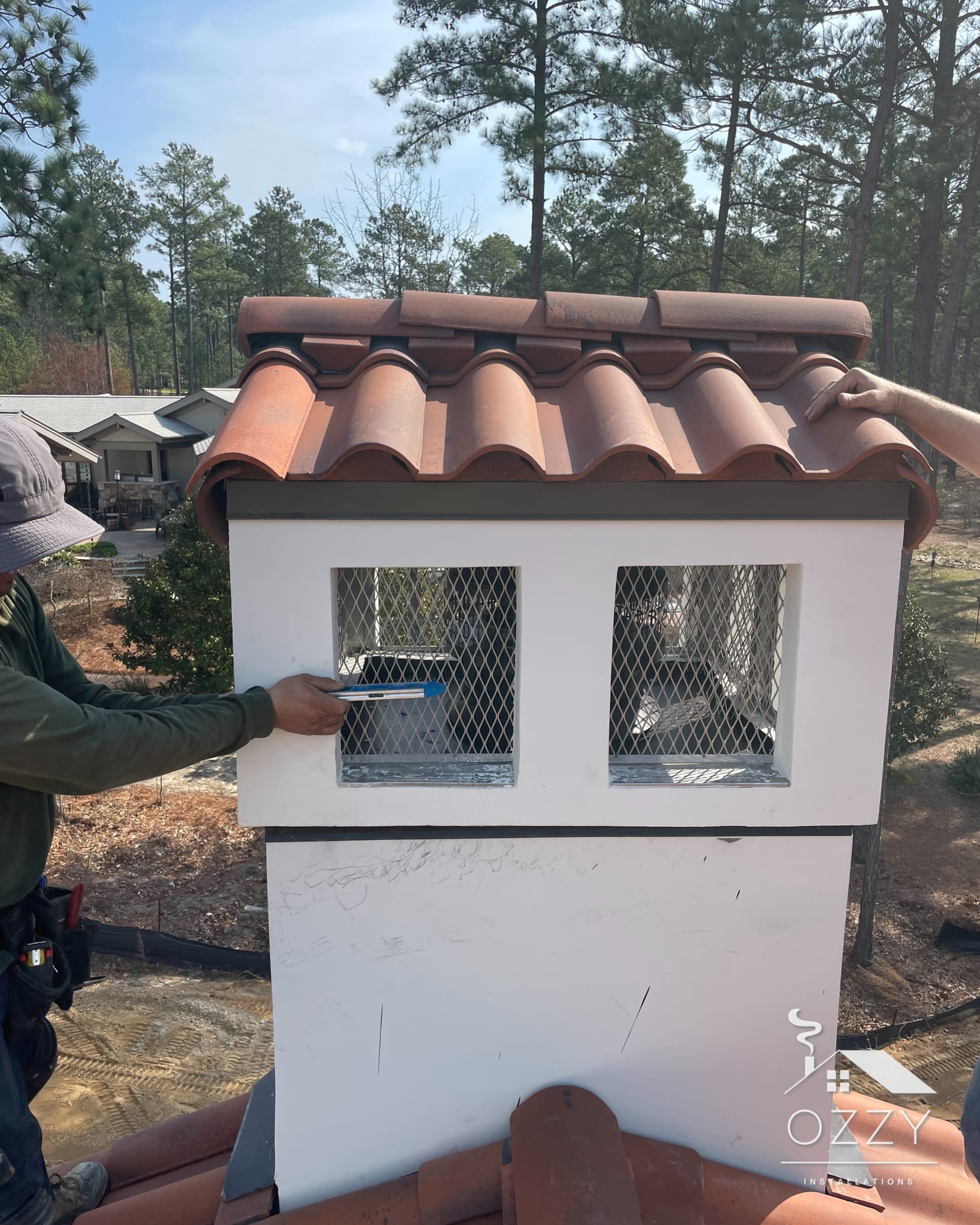 White chimney with mesh openings and a clay tile cap on a tile roof