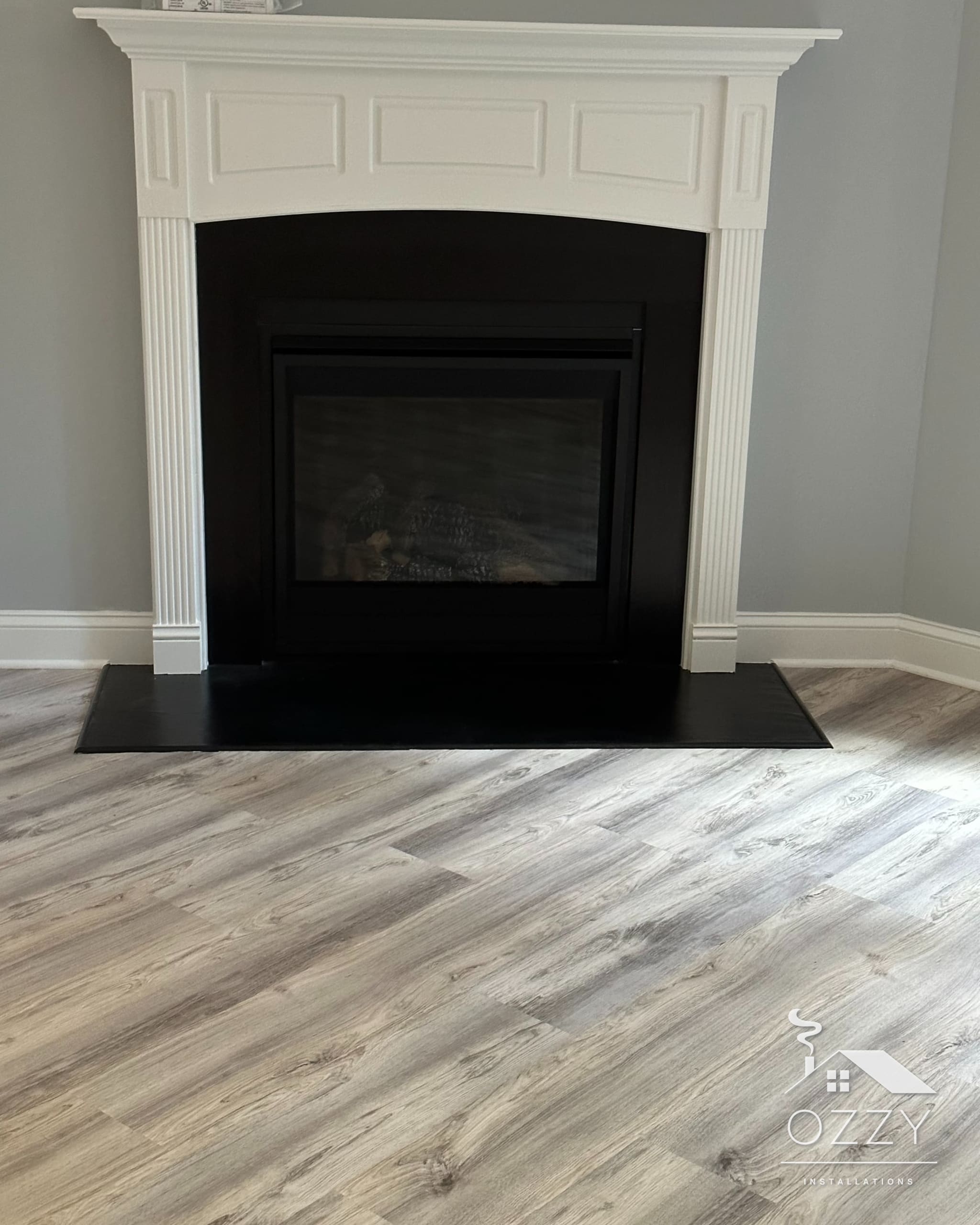 White painted mantel with a black surround and hearth on a light wood floor