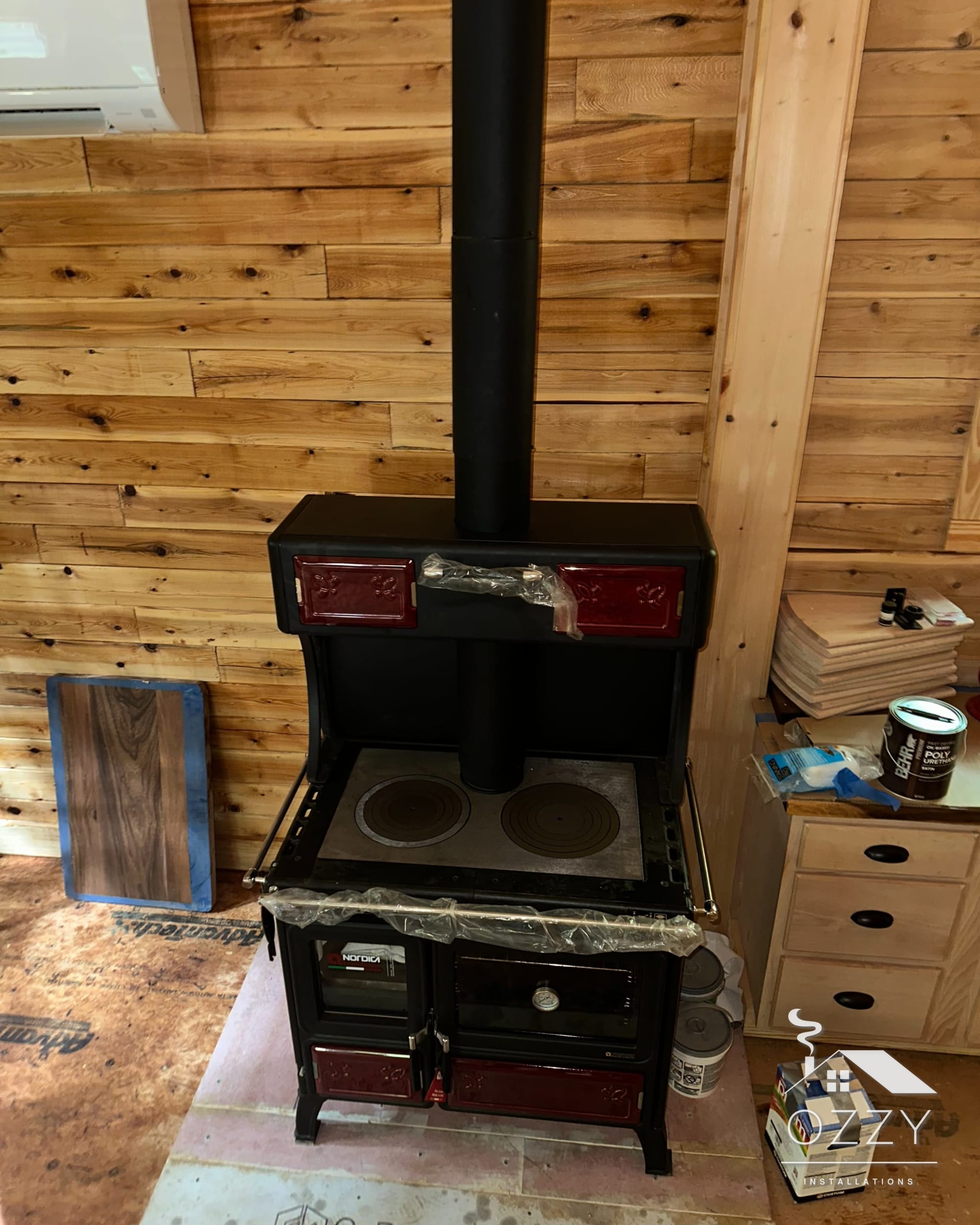 Black wood stove with stovepipe in a pine-paneled cabin