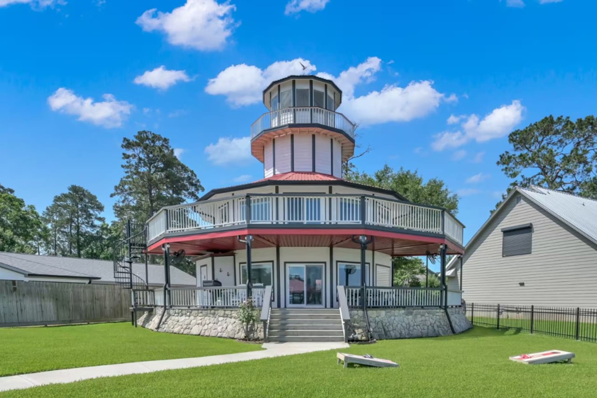 White lighthouse home with a wrap-around deck and red roof on a green lawn in Livingston, Texas