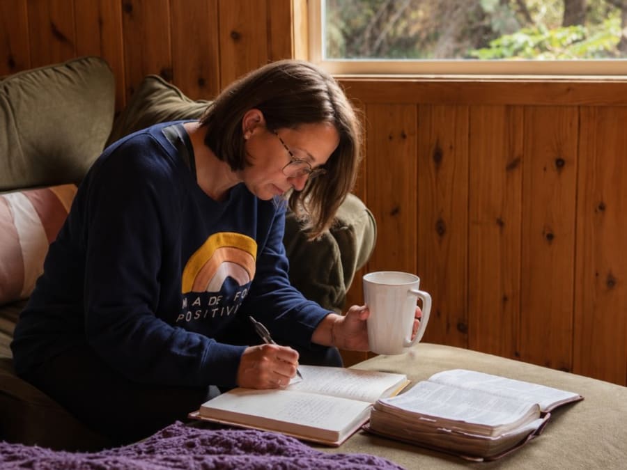 A woman journaling with coffee on a couch beside a forest window