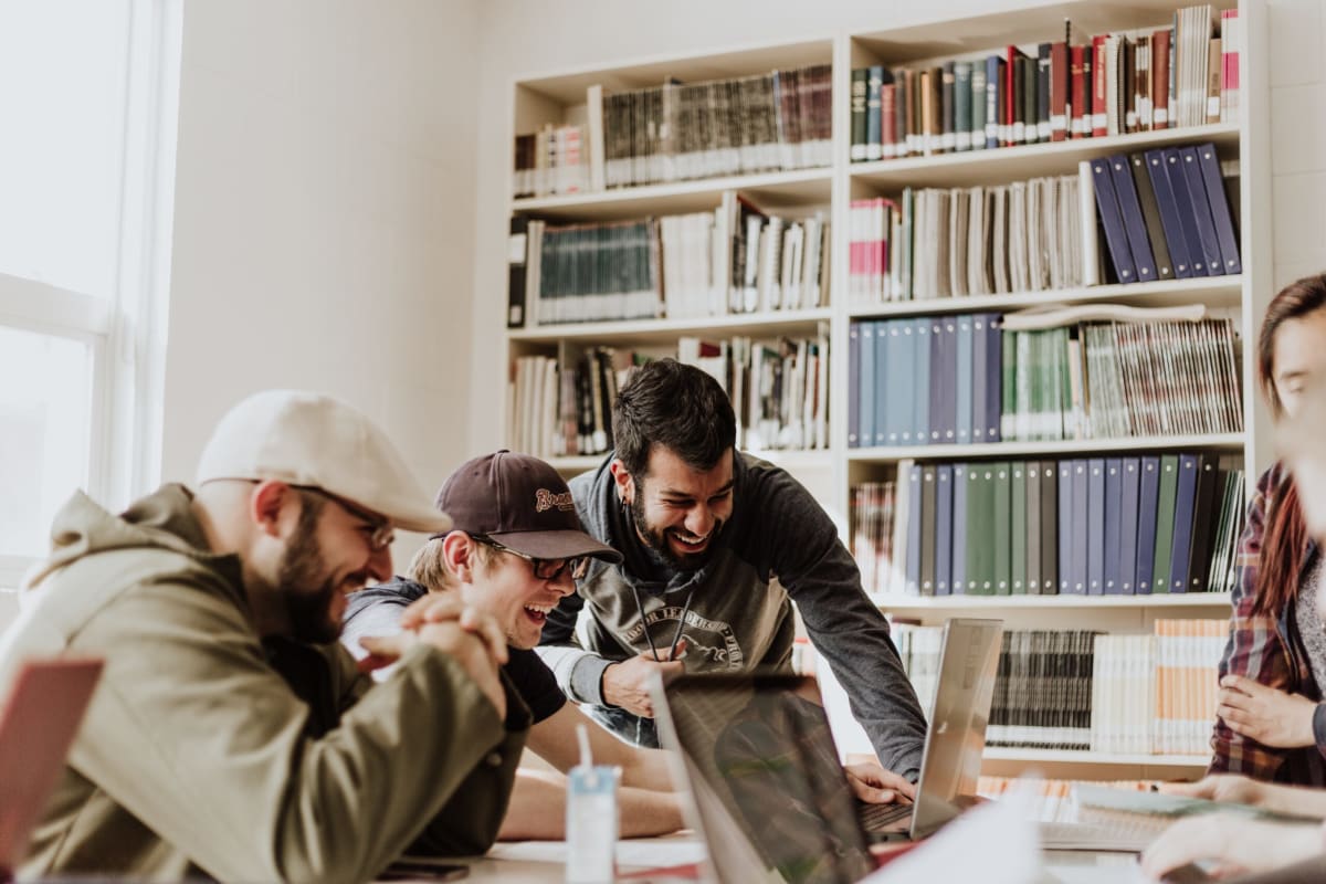 Cultural fit | Group of coworkers laughing together in a room that has a back wall full of books.