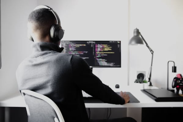 Hire Python developers | Man sitting at a computer in a black shirt and headphones, shot from behind, against a white background