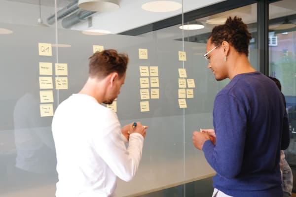 Hire a SaaS engineer | Picture from behind of two men making quarterly plans with post-it notes on a glass wall.