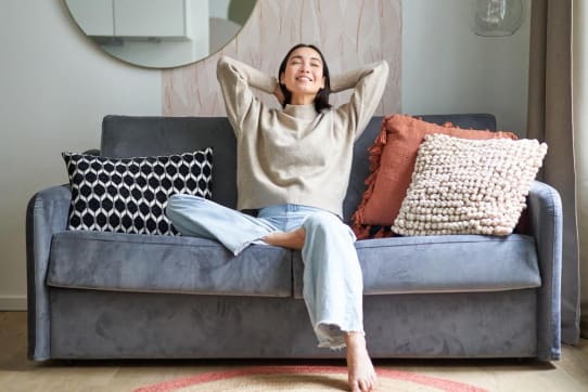 Woman relaxing on a cozy sofa with textured pillows showing decorating apartment ideas that blend comfort and style. | Sohnne® Woman relaxing on a cozy sofa with textured pillows showing decorating apartment ideas that blend comfort and style.