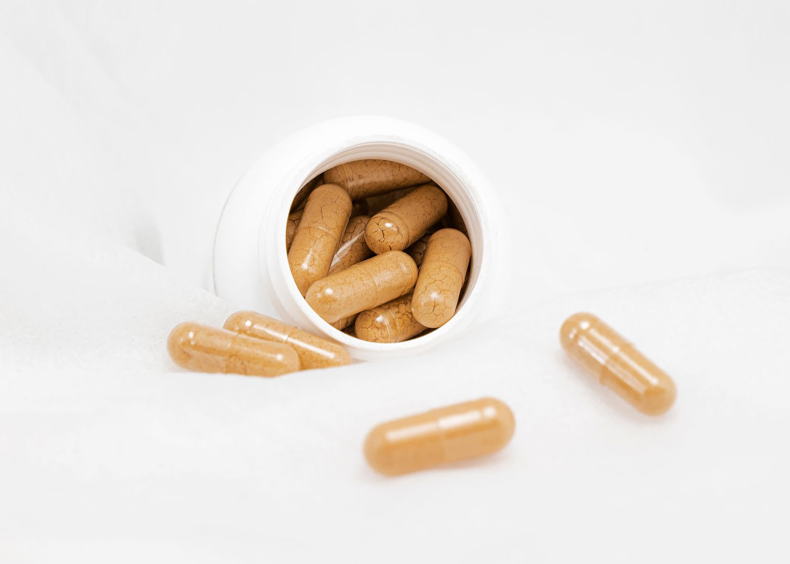 Tan capsules spilling from an unlabelled white bottle onto a white surface.