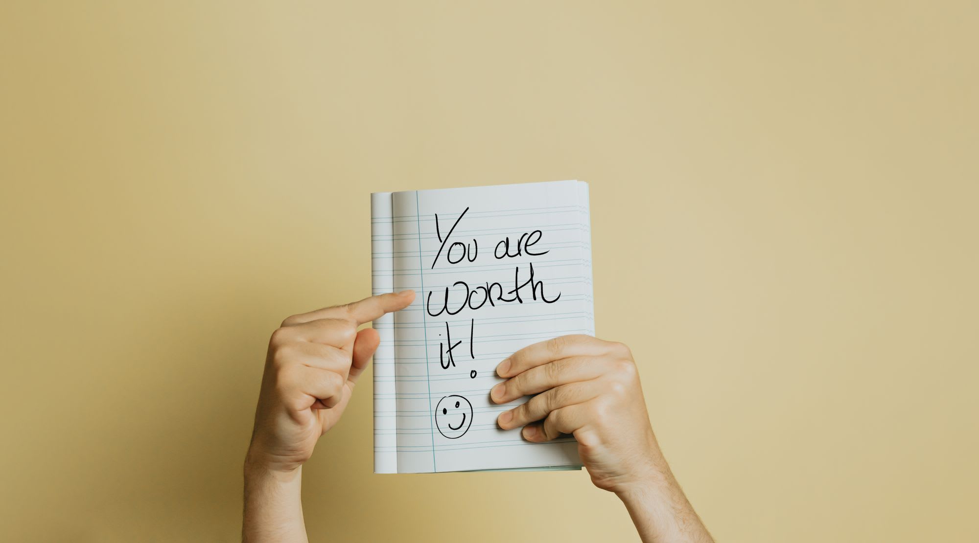 Deux mains tiennent un carnet ouvert avec "Vous en valez la peine !" 😃