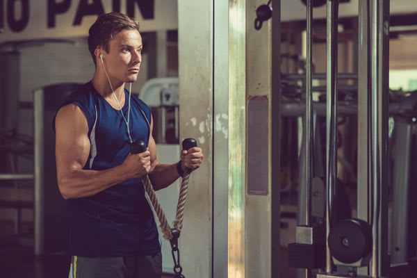 Portrait shot of handsome muscular man listening to music in headphones while doing exercise for triceps at modern gym