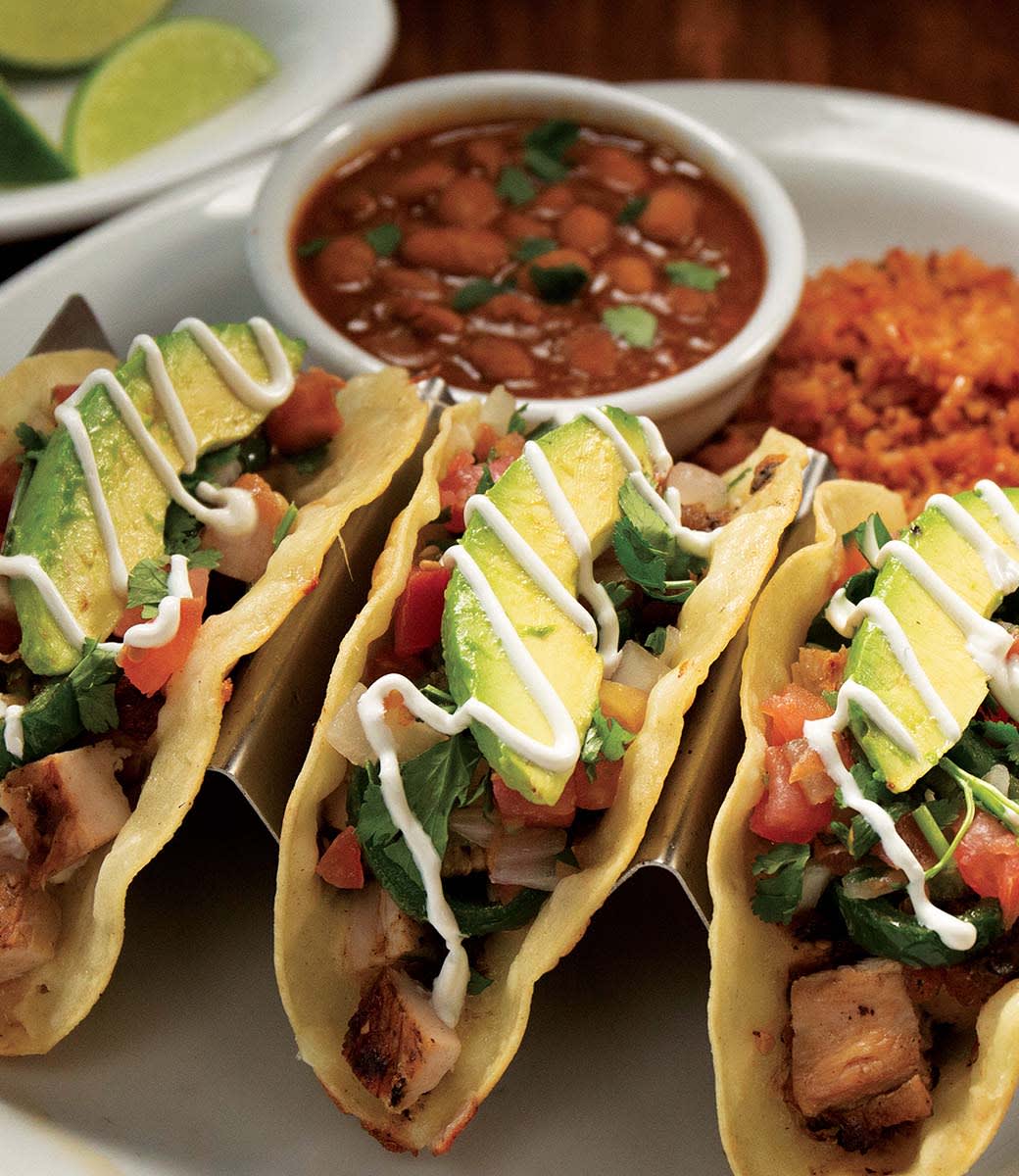 Three street tacos in tortillas topped with avocado slice