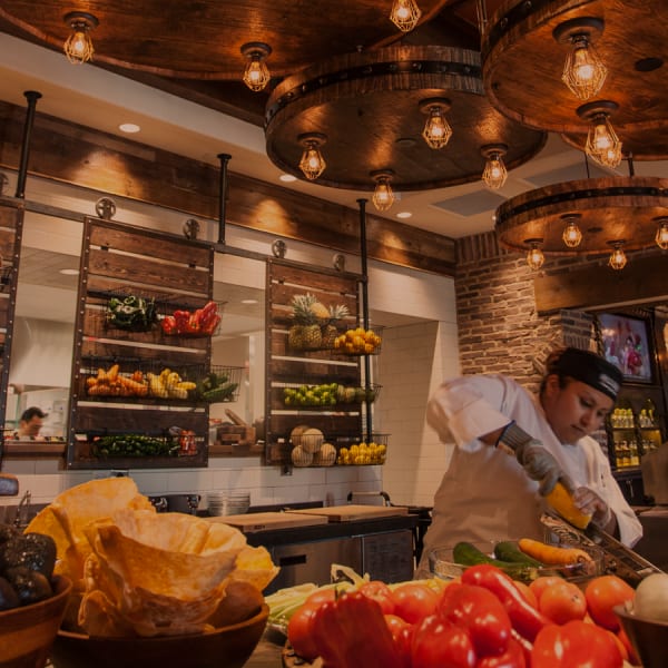 chef cutting fresh vegetables in front of a wall of fresh vegetables and fruits