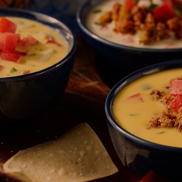 Three bowls of queso with tomatoes and ground beef on top.