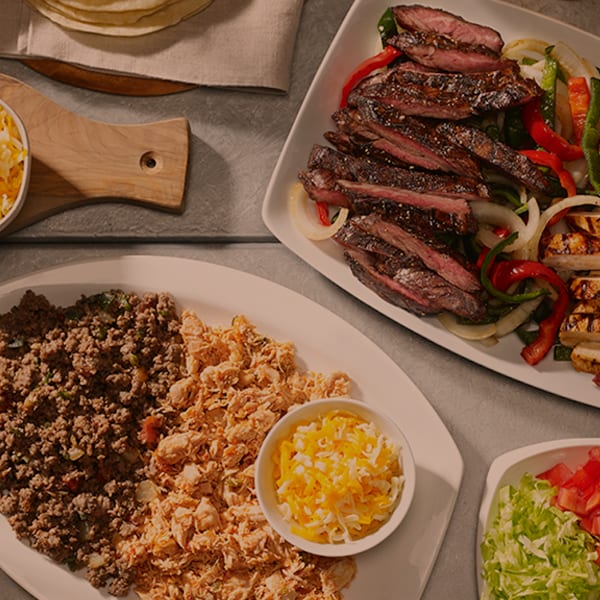 Ground beef, shredded chicken, fajita meats and sides sitting on a table