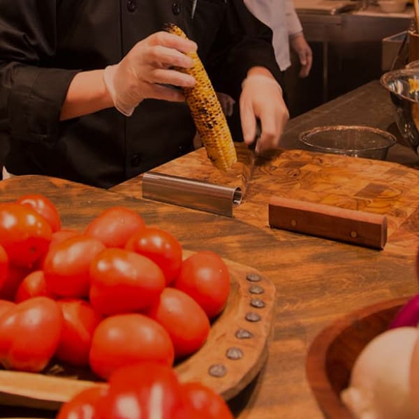 chef cutting corn on a cutting board with tomatoes