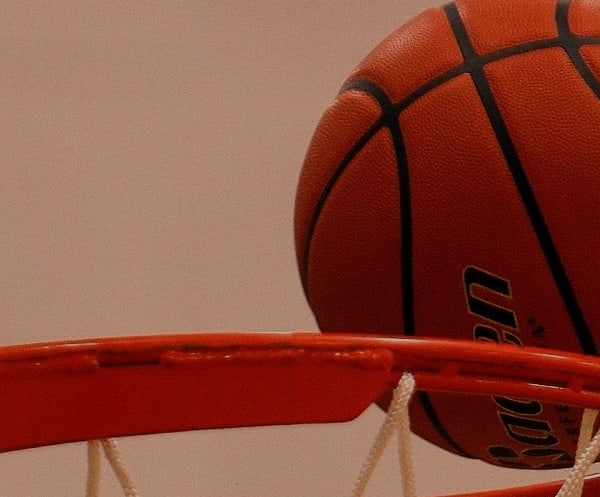 Basketball sitting on the rim of the basketball goal.